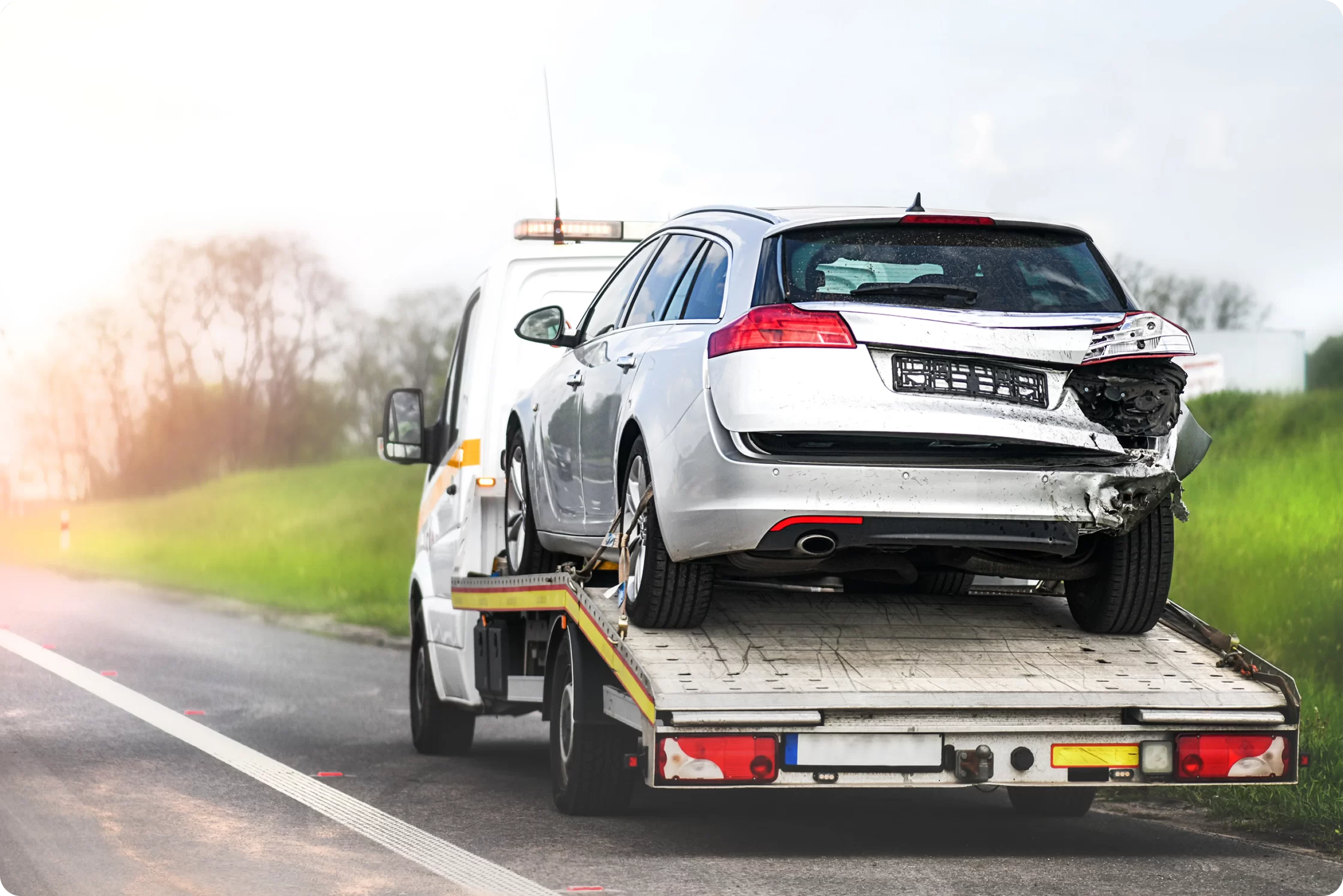 A damaged white SUV is on a flatbed tow truck after a car accident, with visible rear-end damage on the vehicle.