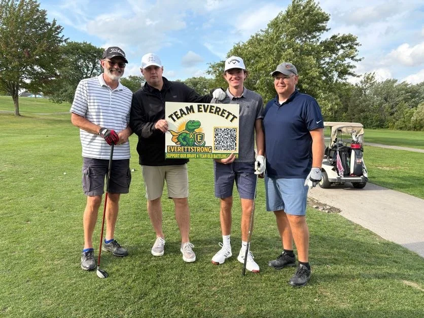 Four men on a golf course holding a sign that says "Team Everett" with a QR code, supporting Everett. Two of the men are holding golf clubs, and there is a golf cart in the background.