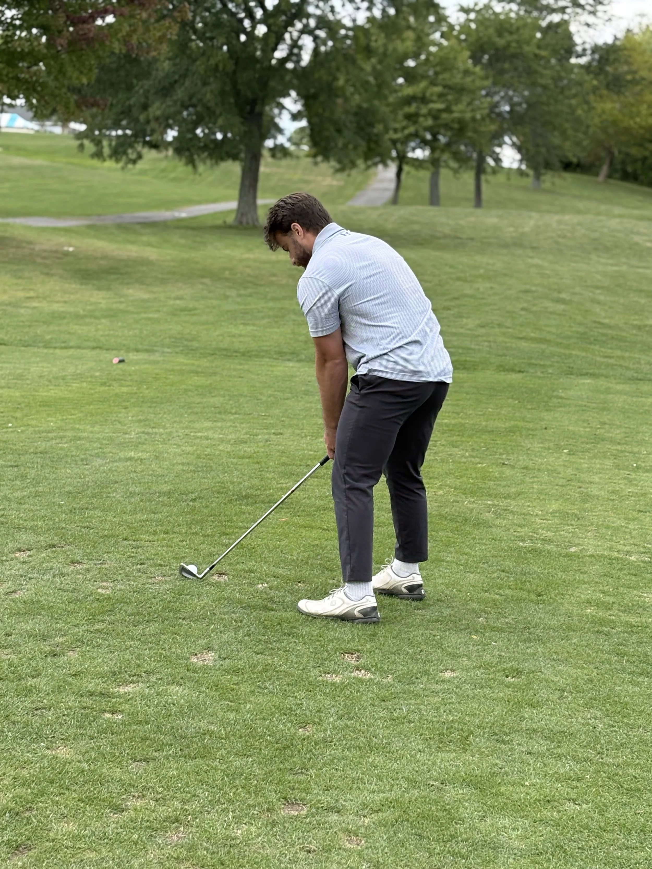A man is preparing to hit a golf ball on a golf course with green grass and trees in the background.