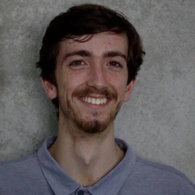 Daniel Jochem, smiling in-front of a white background with a blue shirt.
