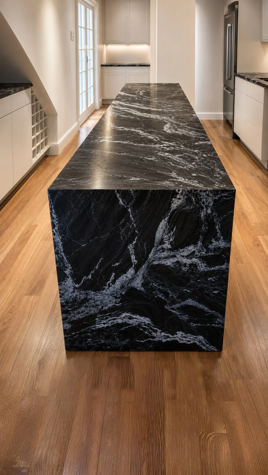 A black marble kitchen island with white veining in a modern kitchen with light cabinets, wood flooring, and stainless steel appliances.