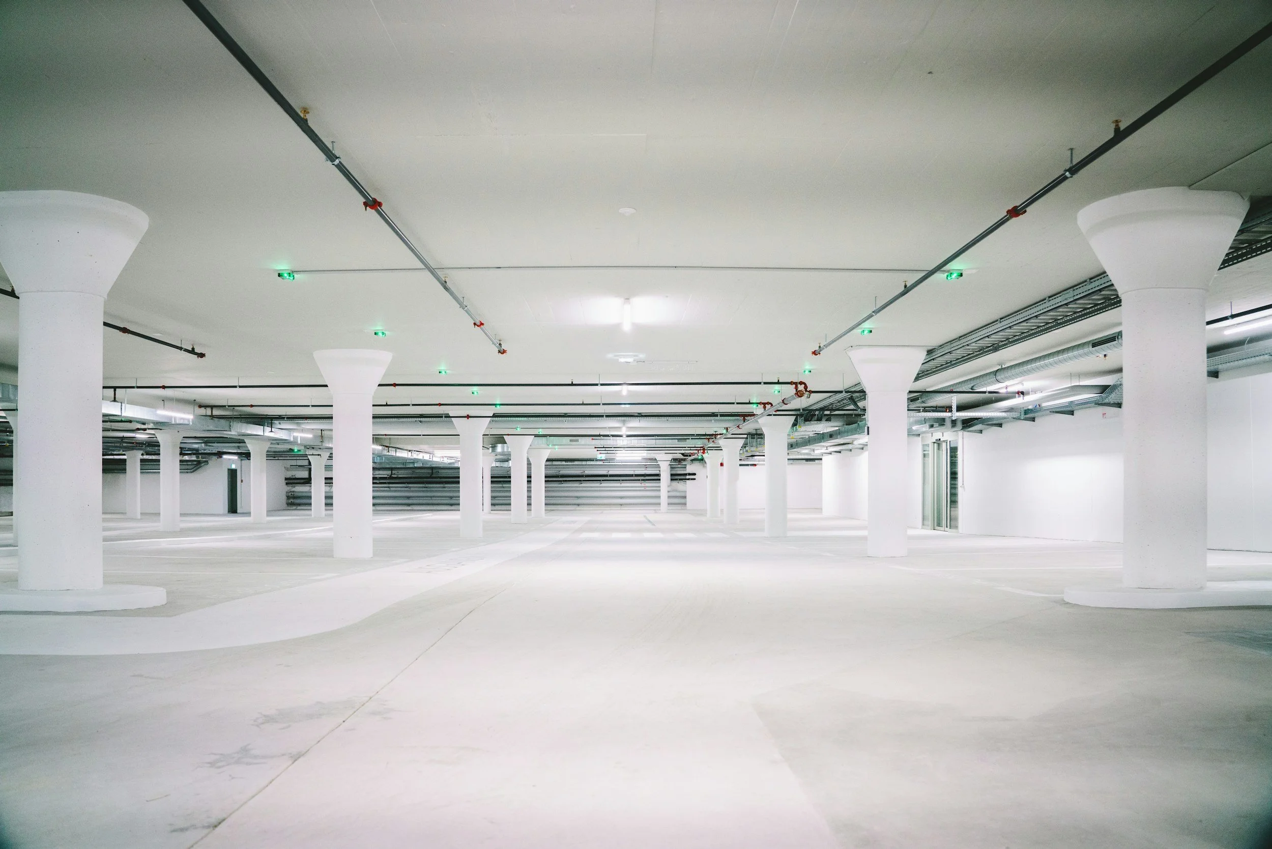 Empty indoor parking garage with white columns and overhead lighting.