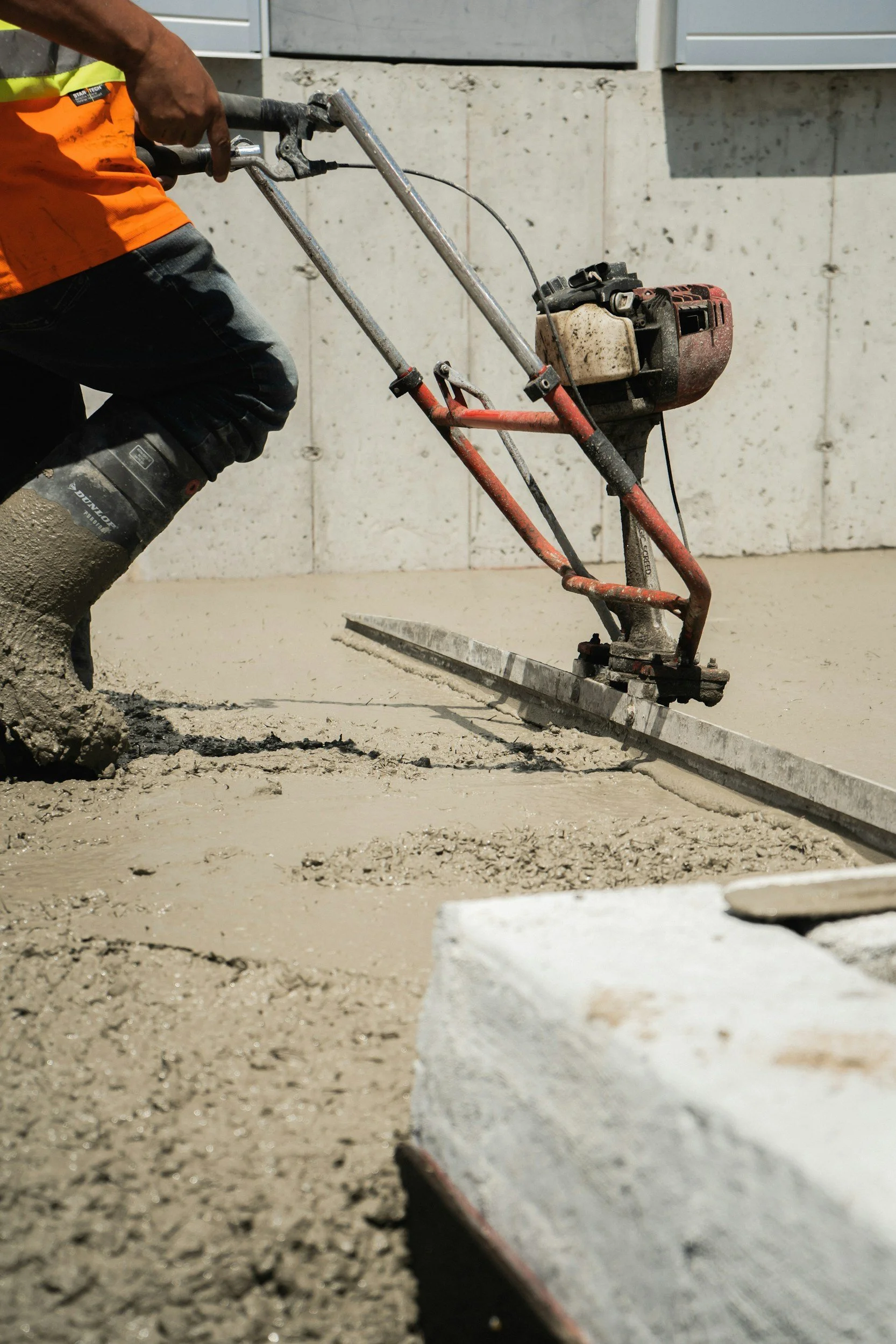 Concrete slab foundation on a construction site with surrounding dirt and grass, and trees in the background.