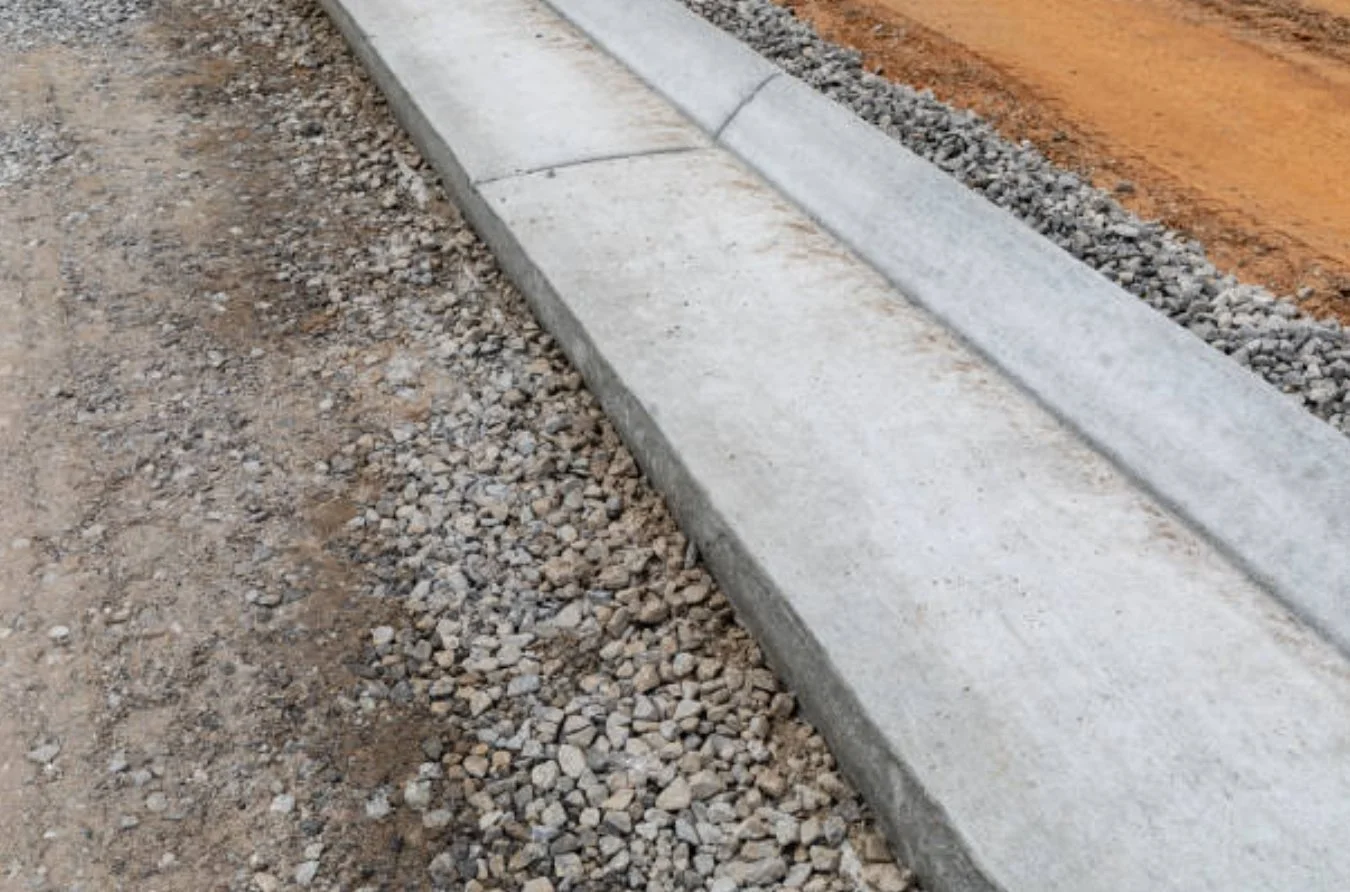 Close-up of a concrete curb along a gravel and dirt roadside.