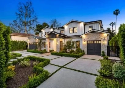 Modern two-story house with white and gray exterior, black garage door, and landscaped front yard with pathway and greenery during daytime.