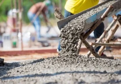 Concrete being poured and spread on a construction site with workers in the background.