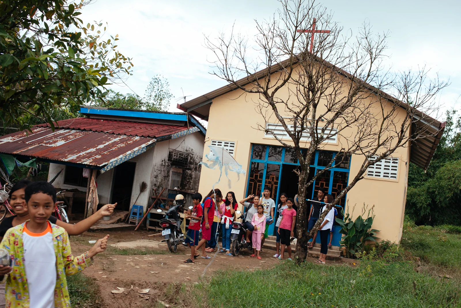Two boys attempt to fly home made kites as some Alongsiders and their little brothers and sisters gather in front of the church. (Kampong Saom, Cambodia)