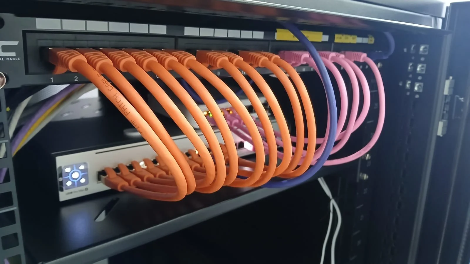 Network server rack with multiple orange and pink Ethernet cables connected to switches.
