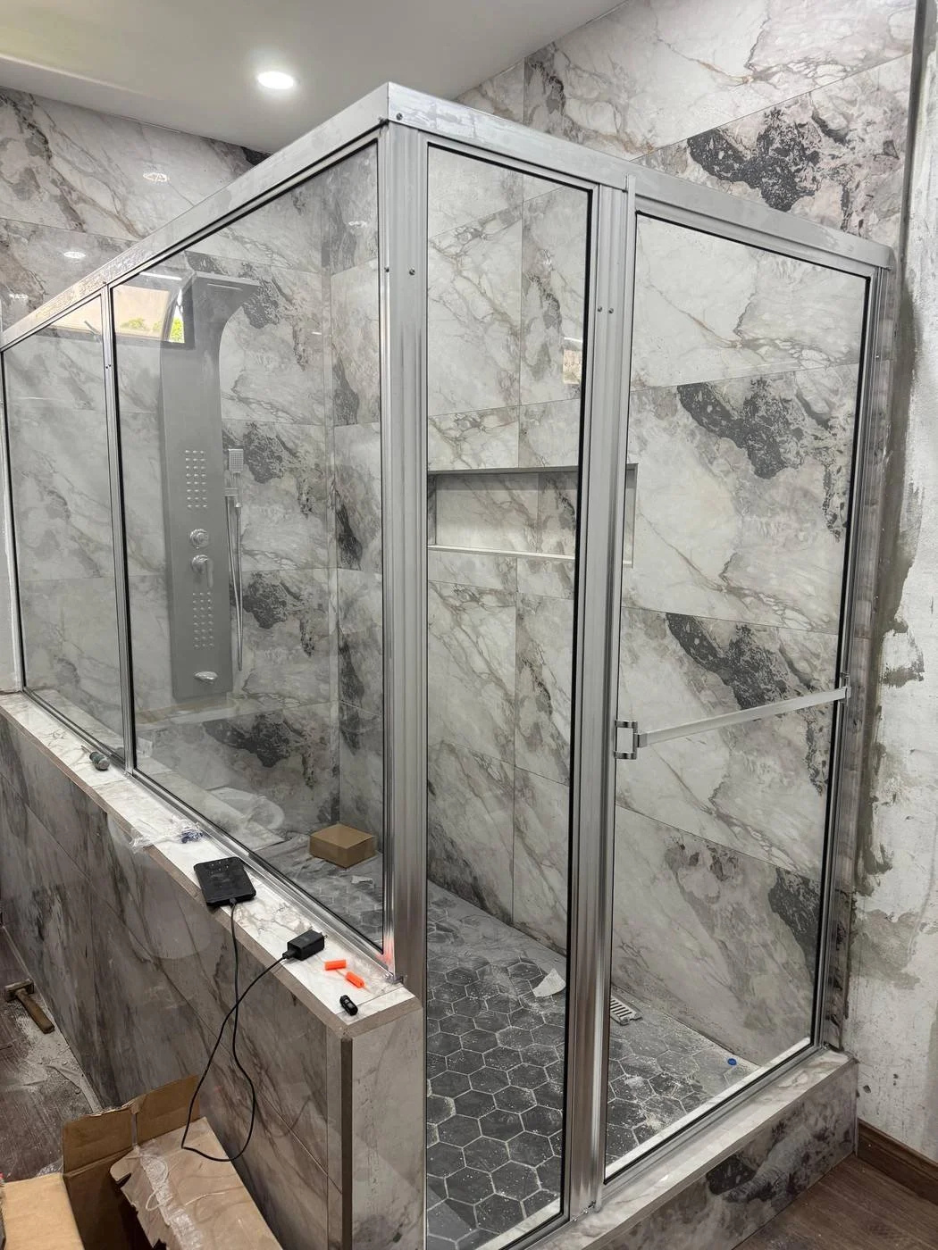 Newly installed glass shower enclosure with marble walls and black hexagonal floor tiles.