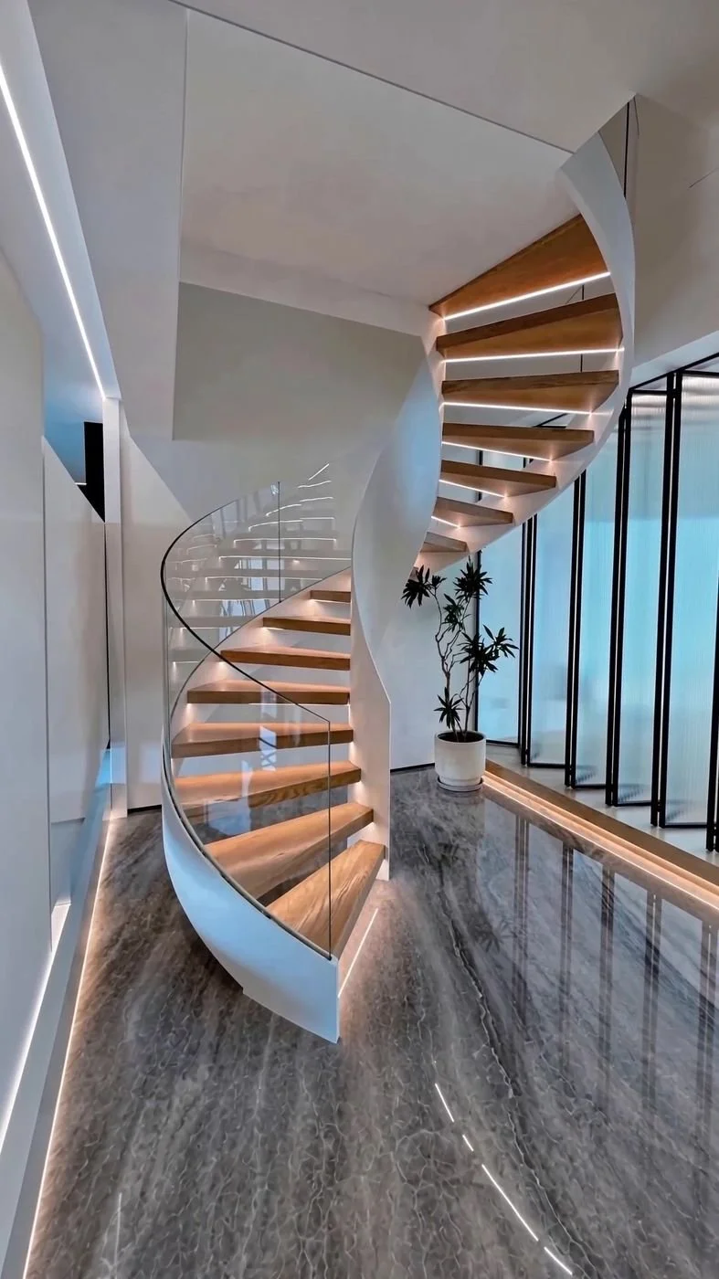 Modern interior staircase with wooden steps, glass railing, and LED strip lighting, in a bright room with marble floor and potted plant near large windows.