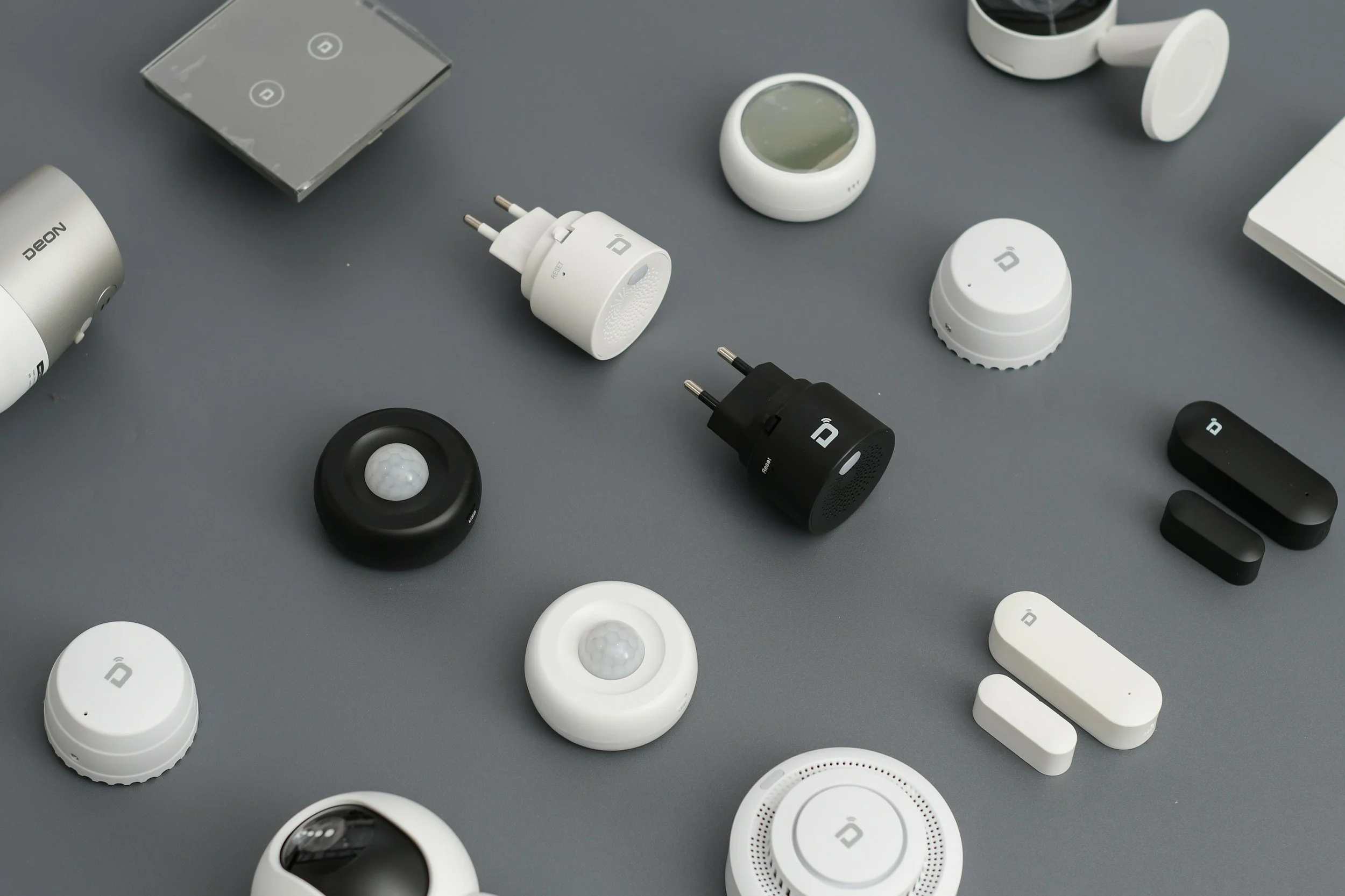 Various smart home gadgets and devices on a gray surface, including speakers, chargers, and sensors.