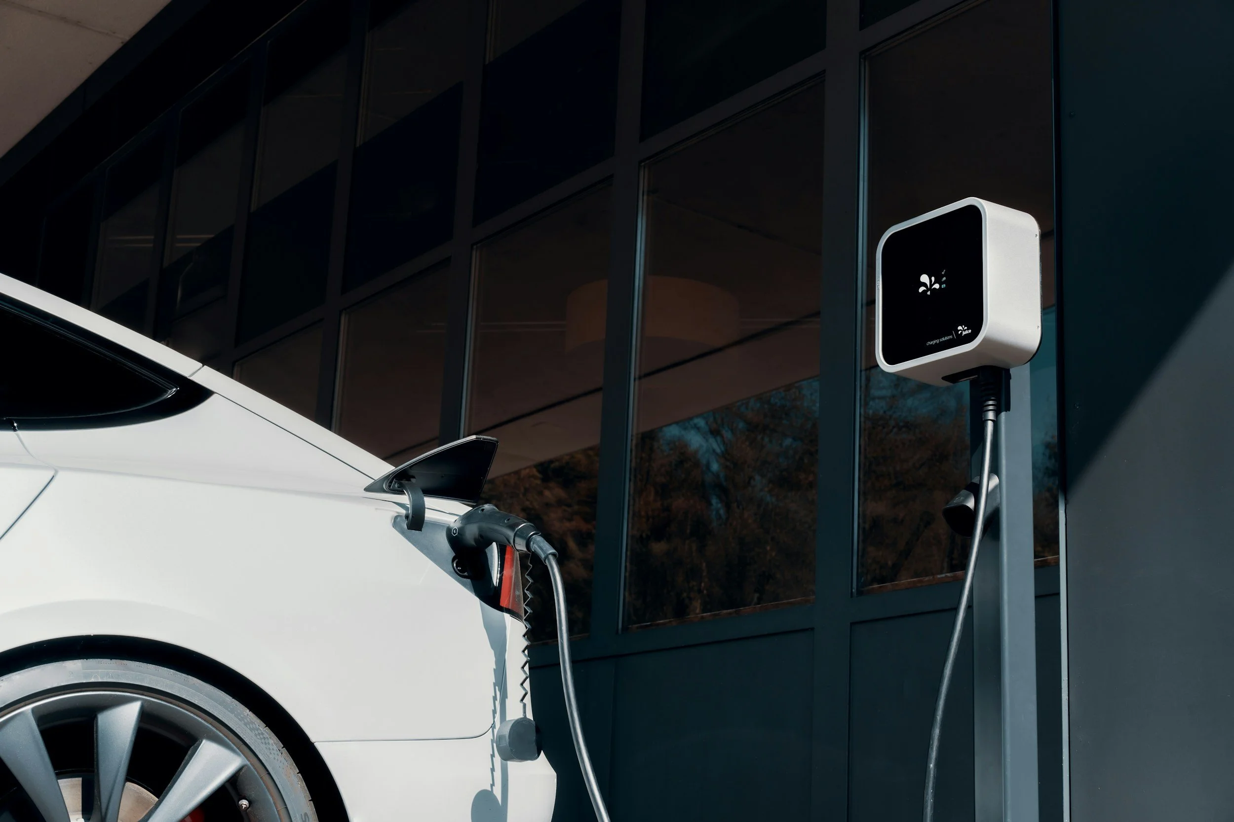 Electric car charging at a charging station outside a modern building with glass windows.