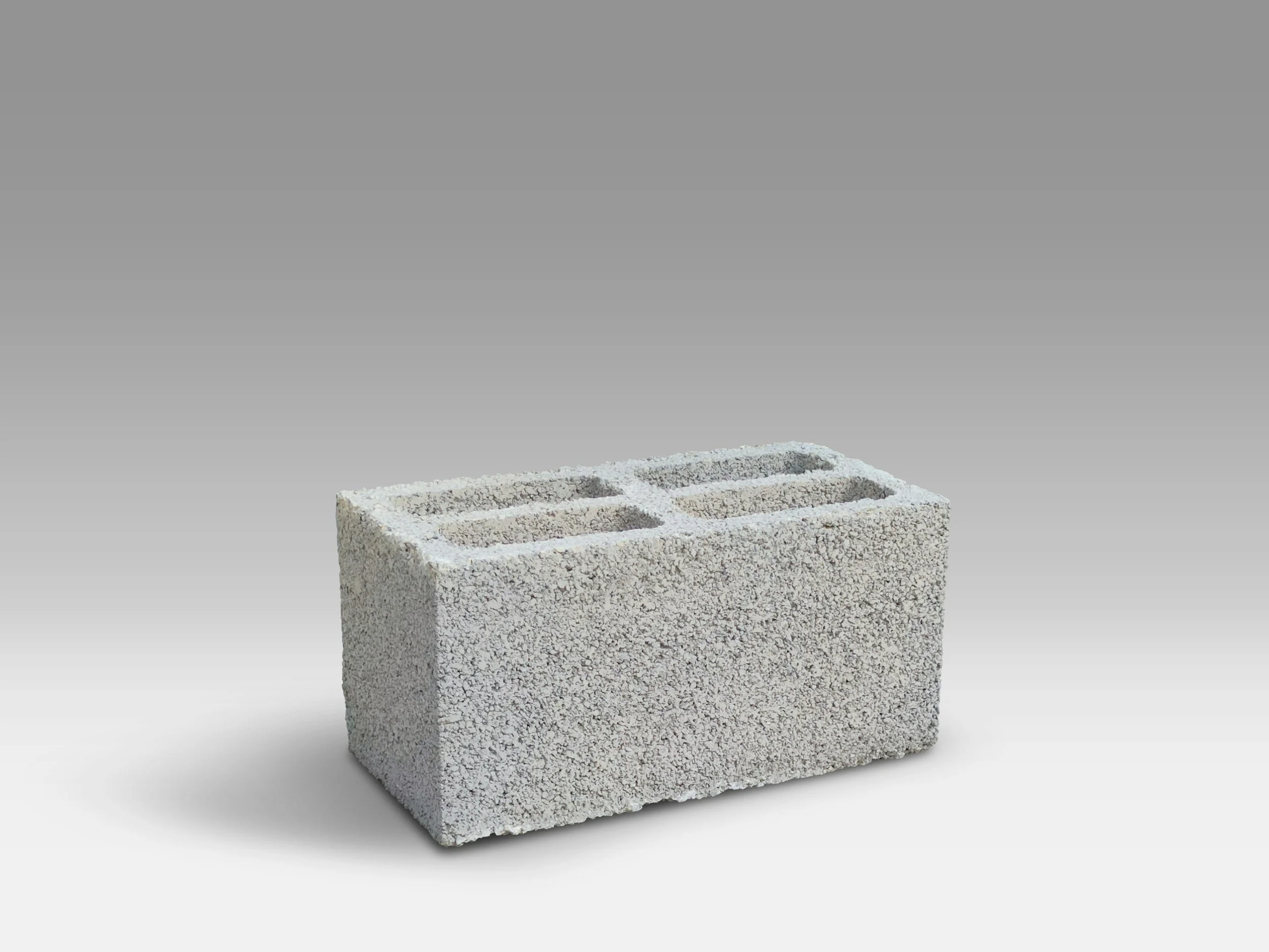 A white foam cinder block with three rectangular hollow sections, placed against a plain gray background.