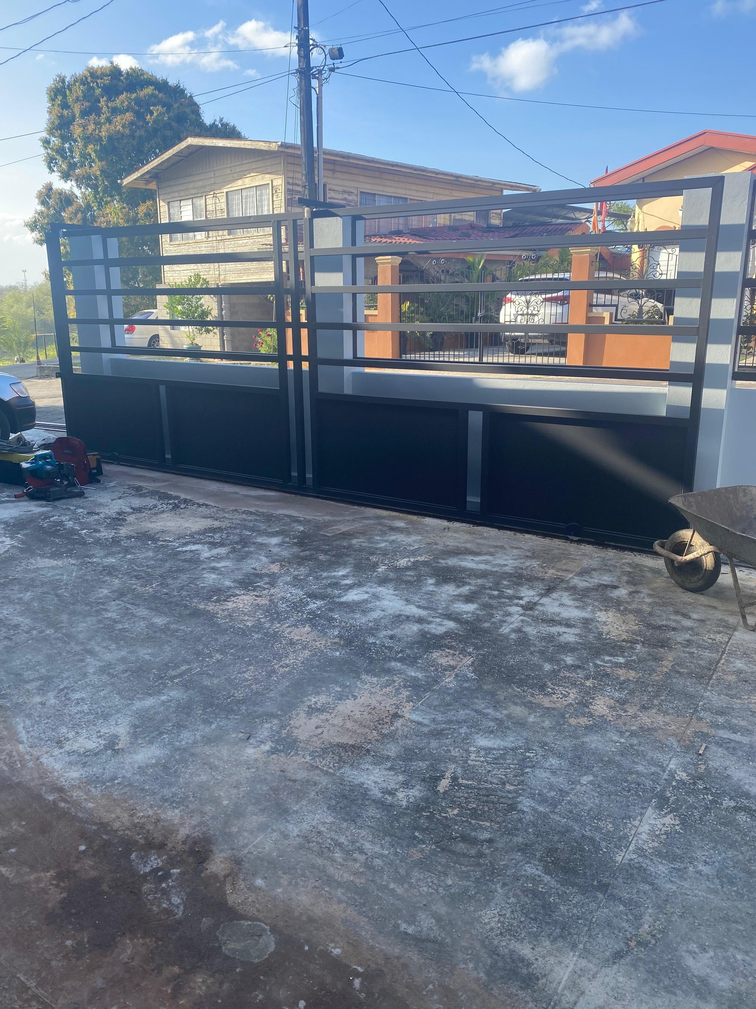 A partially constructed metal and glass gate or fence in front of residential houses on a sunny day.