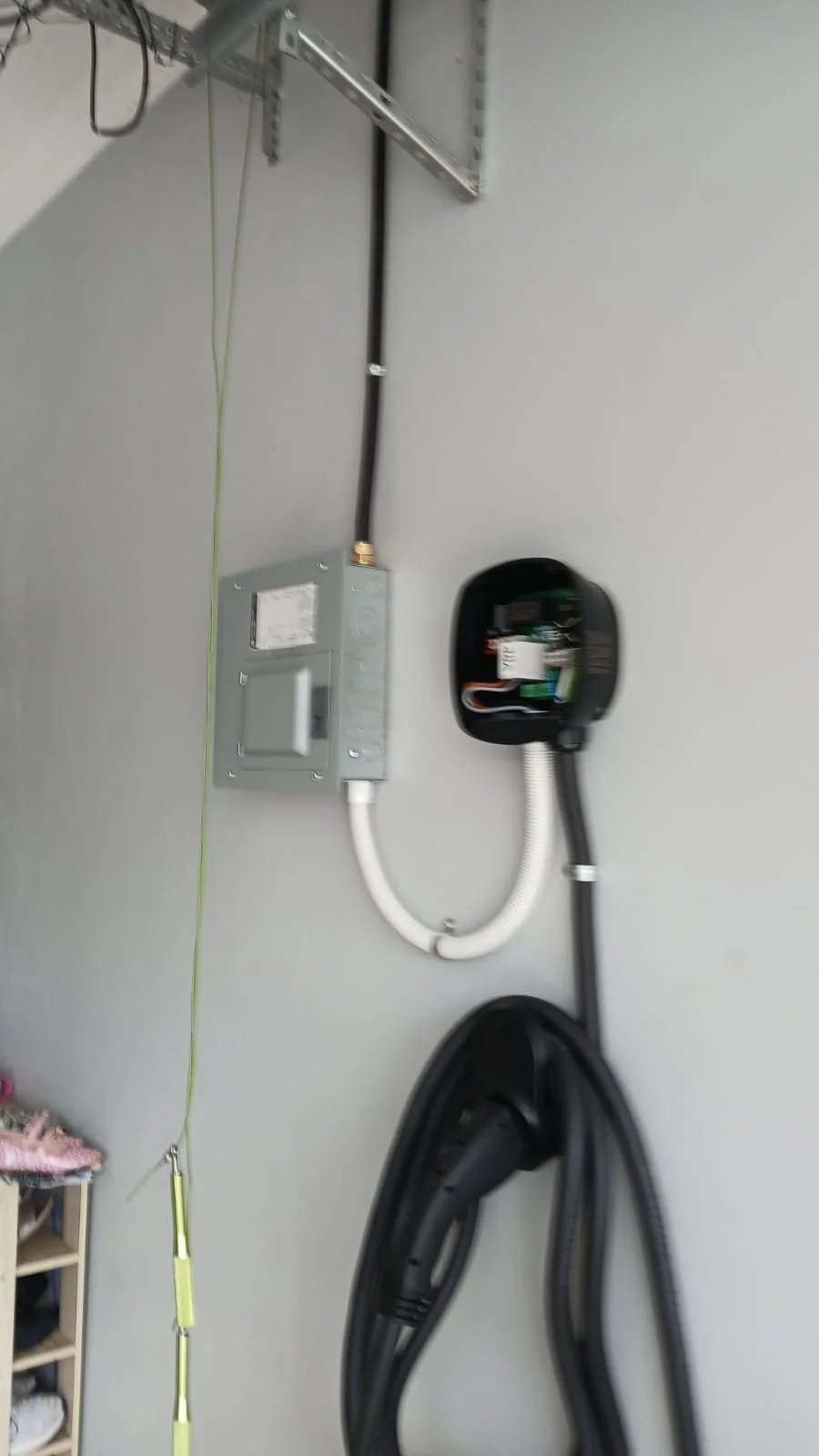 Garage wall with electrical box, black and white hose connected to a vacuum outlet, wall-mounted electrical and garage door wiring.