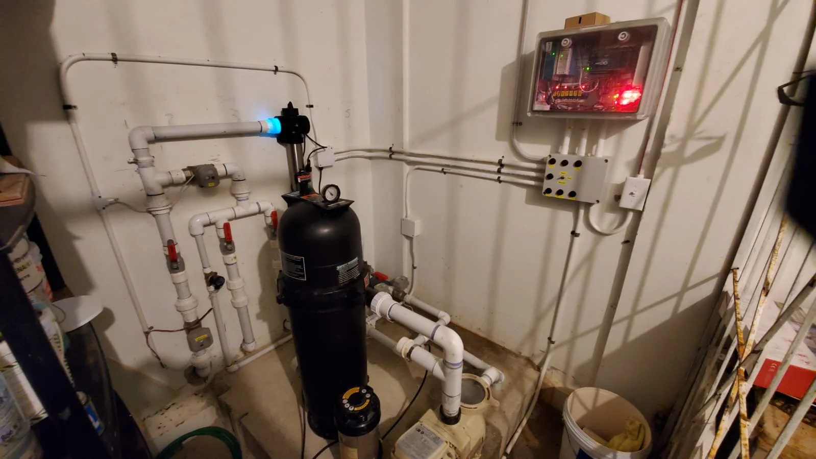Pump system with pipes and gauges in a utility room, with electrical control box on the wall.