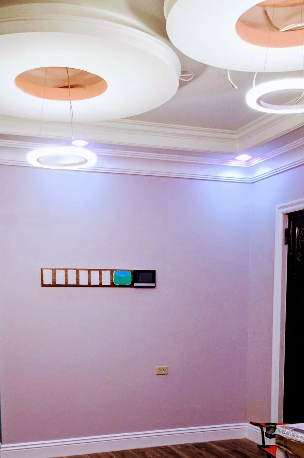 Interior room with decorative ceiling lights, a pastel-colored wall, a power outlet, and a small shelf with colorful objects.