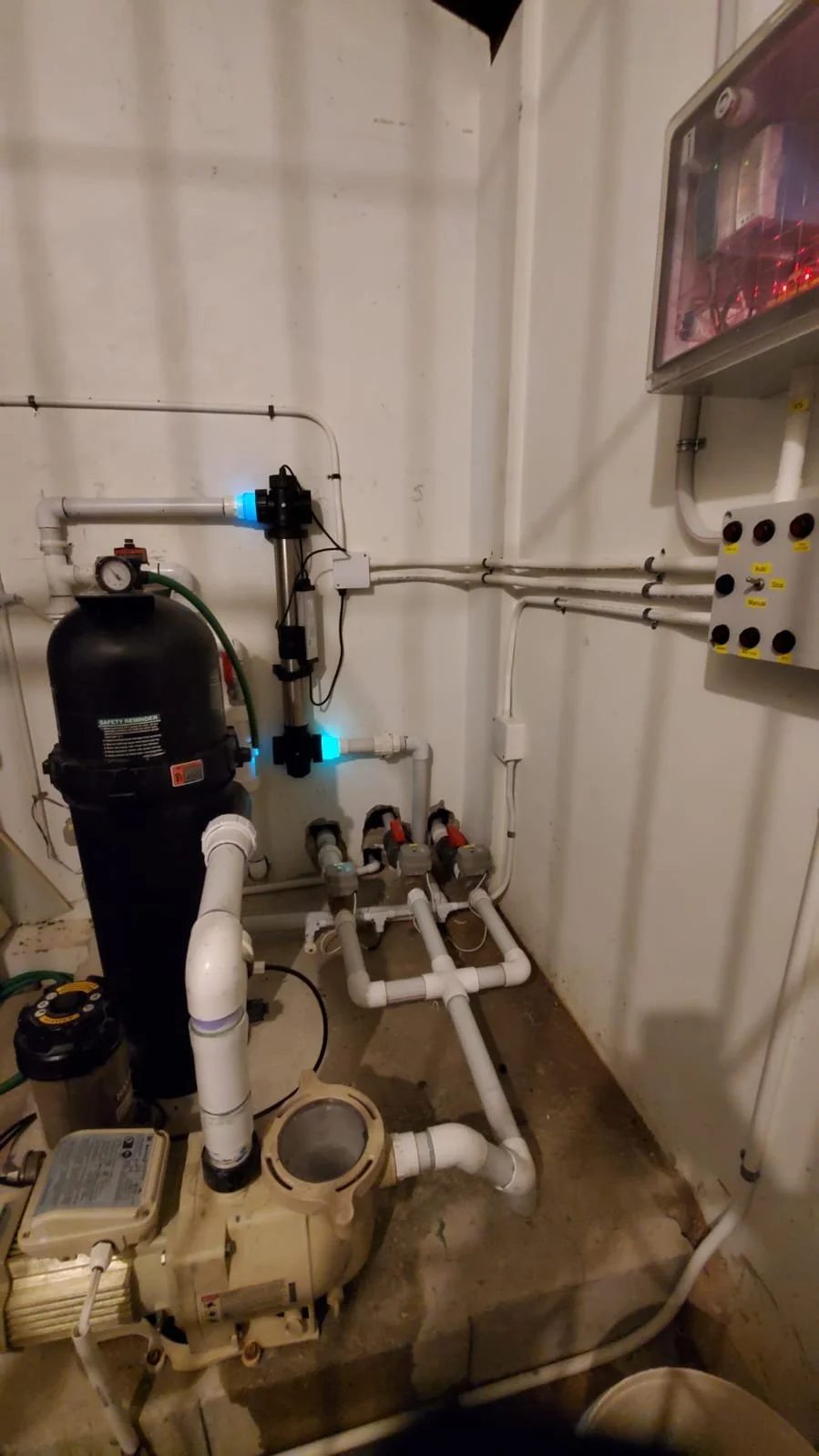 A water filtration system with pipes, gauges, and a black tank, installed against a white wall in a utility room.