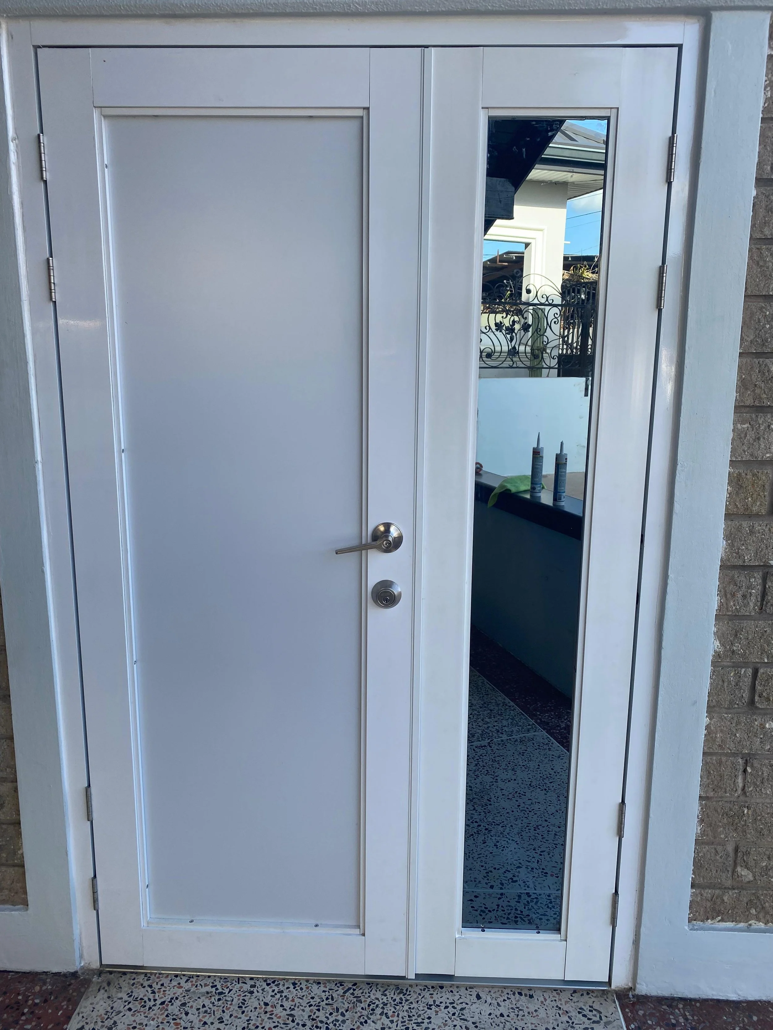 White exterior door with a mirror on the right side, showing an outdoor area with a porch and decorative black metal railing.