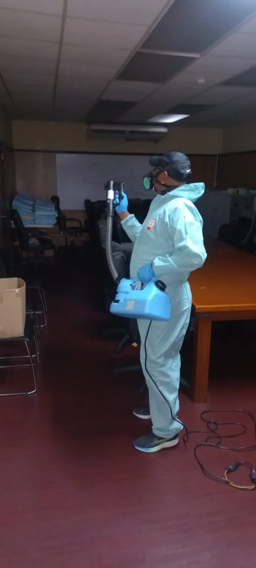 Person in protective gear using disinfectant sprayer in an office room.