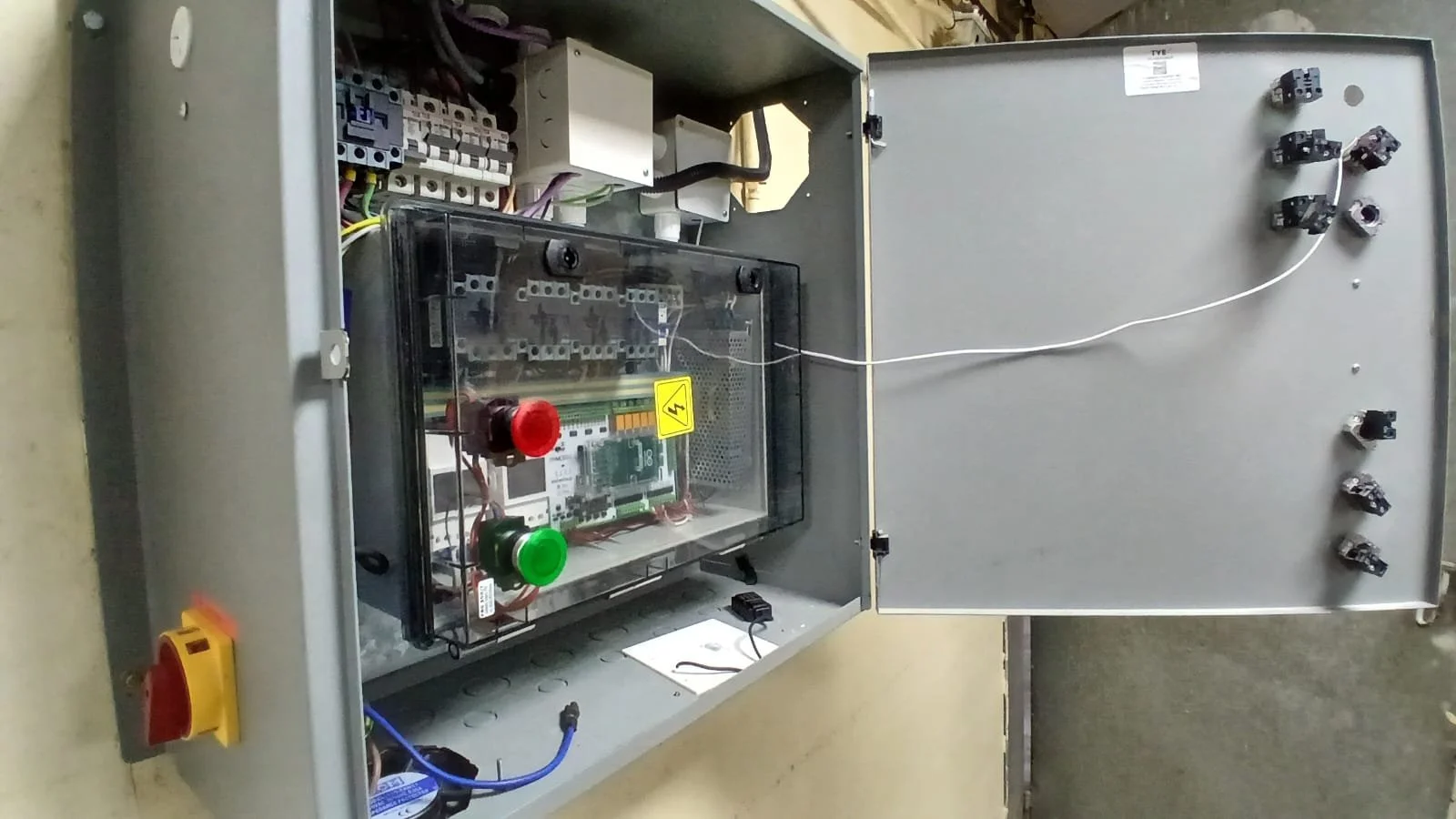 Open electrical control panel with wires, circuit breakers, and components inside; the open door reveals wiring and electronic parts mounted inside the metal box.