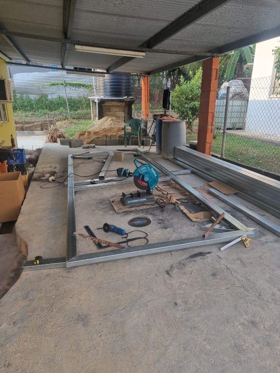 Construction site with metal framing, power tools, and materials for building a structure under a carport or garage.
