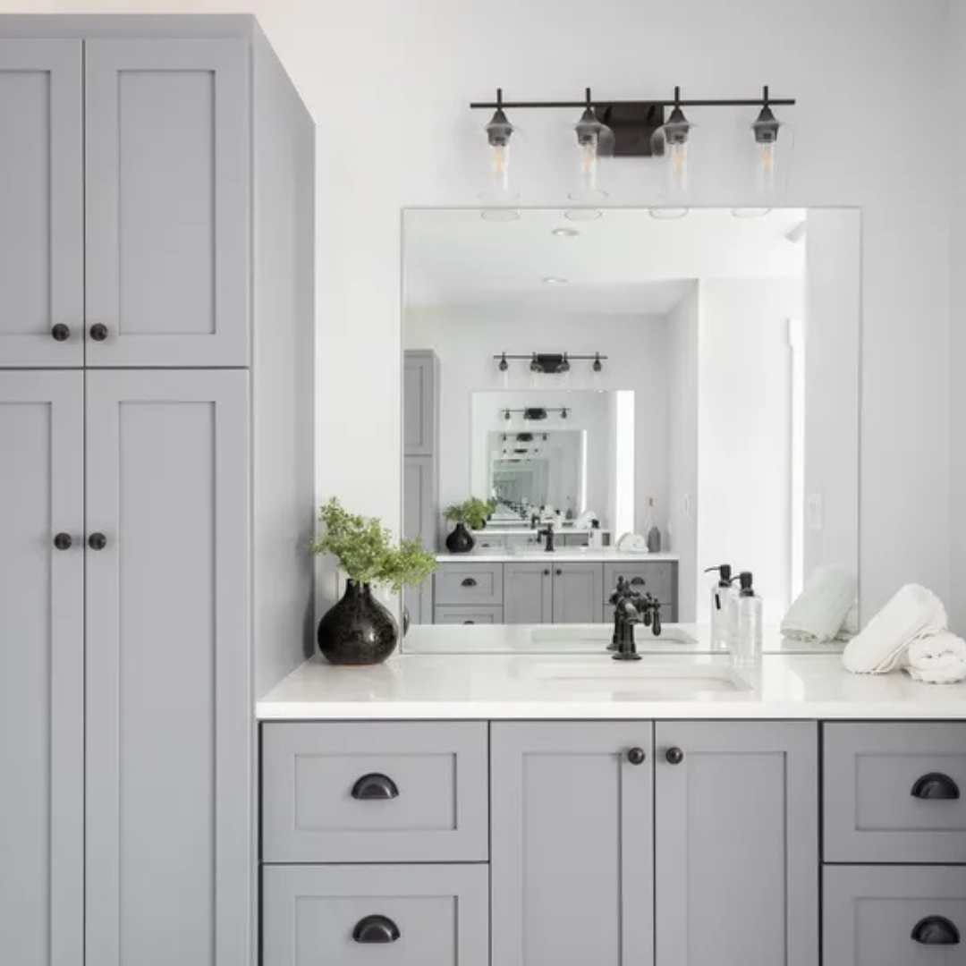 Bathroom vanity with large mirror, black fixtures, white countertop, decorative black vase with greenery, soap dispenser, and neatly folded white towels.