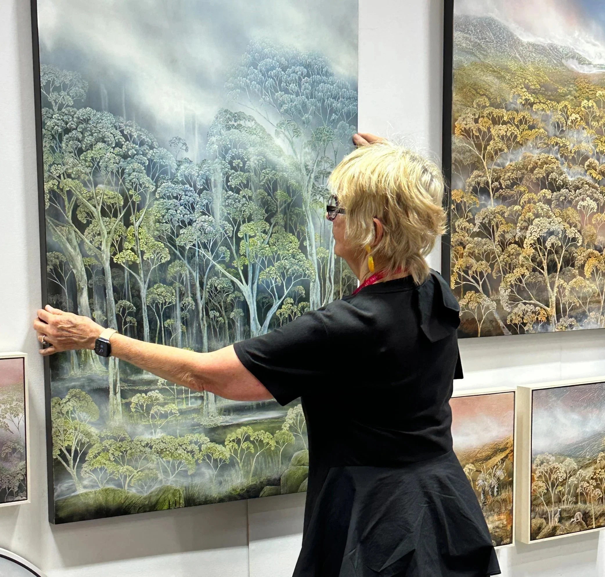 Frances Keevil hanging landscape paintings of trees in an art gallery.