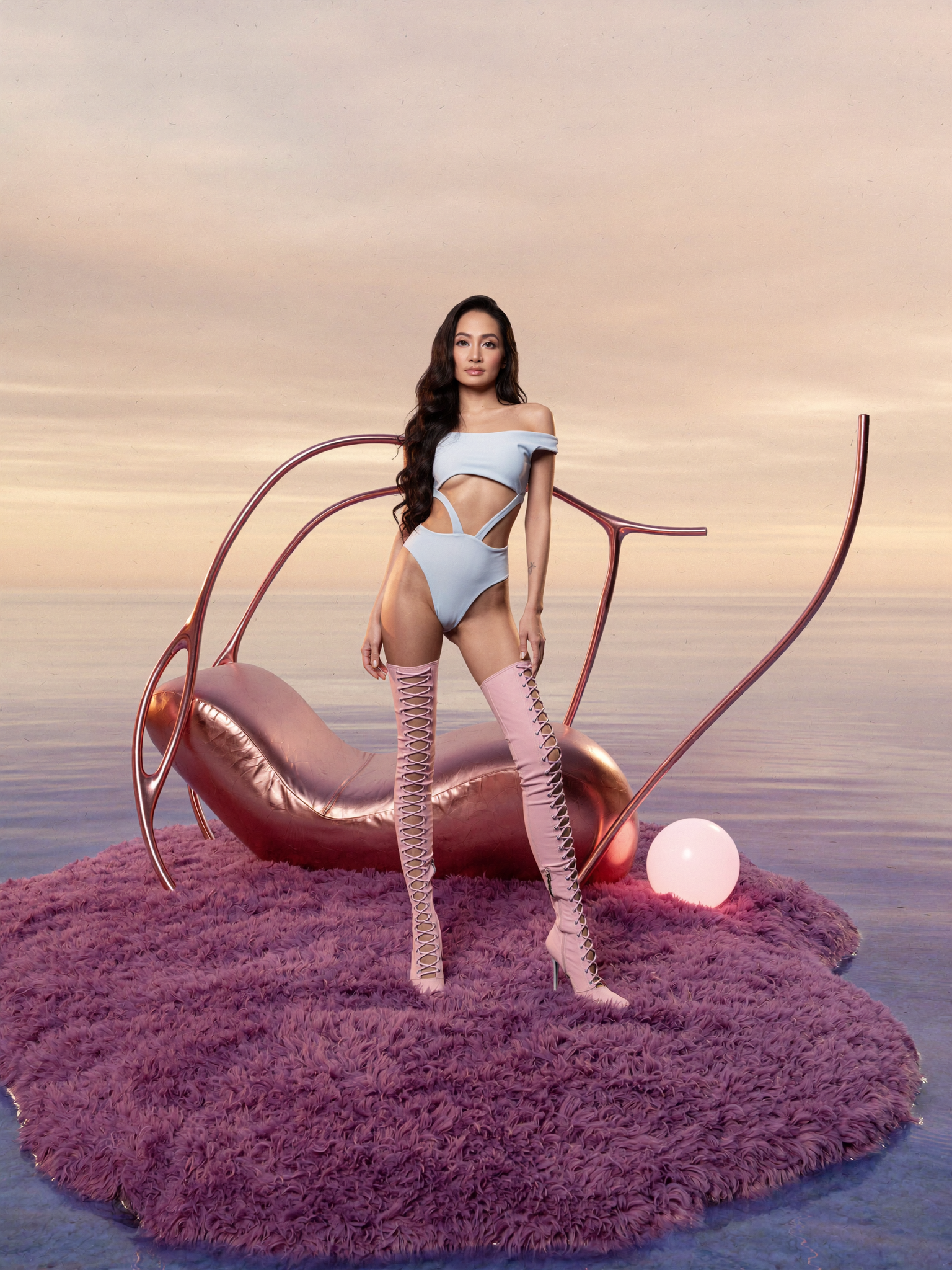 A woman in a cutout and strappy bodysuit with thigh-high lace-up boots standing on a pink shaggy rug in front of a sunset ocean background. She is next to large pink and rose gold stylized swan sculptures with a glowing white orb nearby.