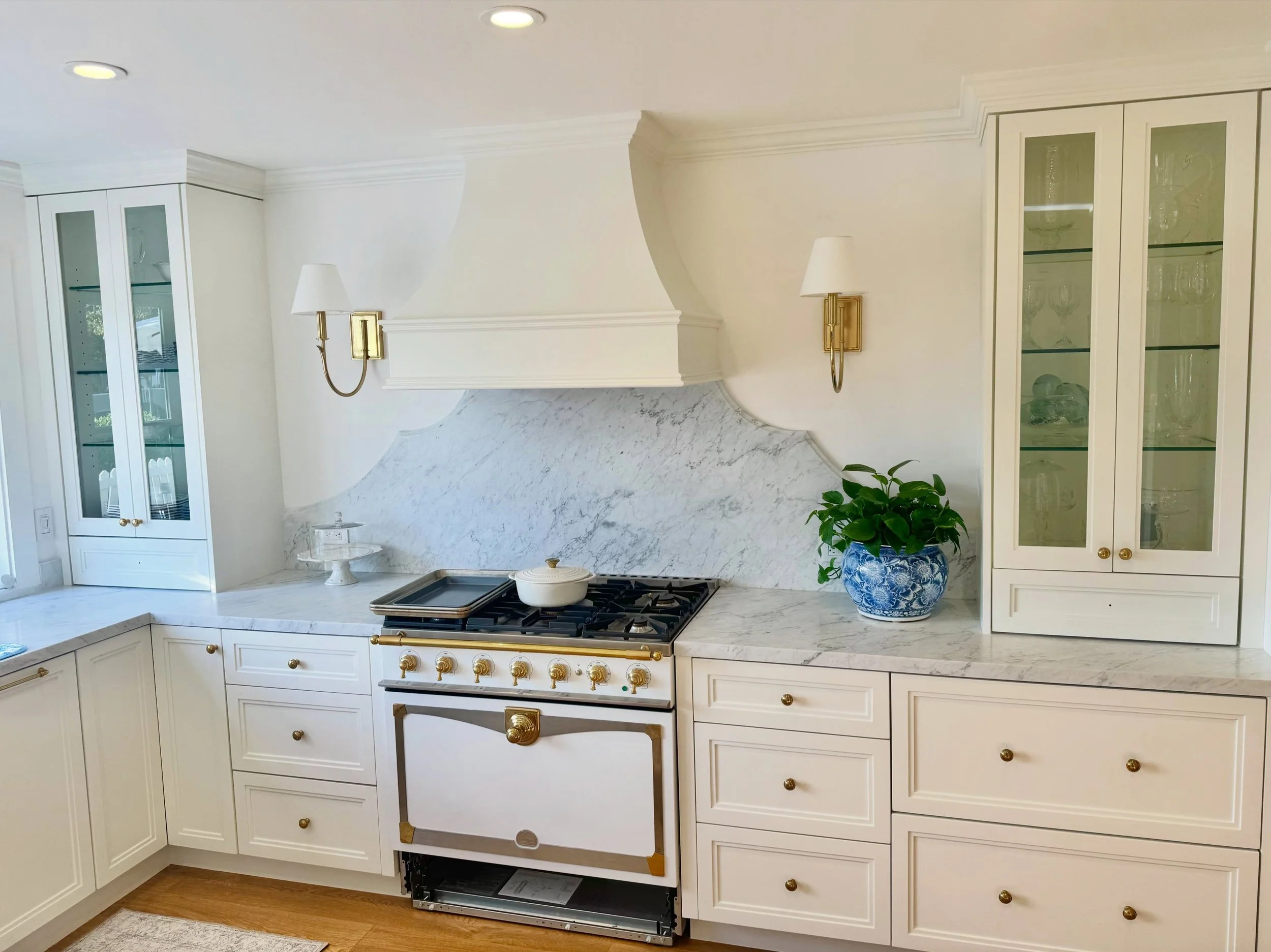 Custom frameless cabinets in full overlay white double shaker, minimal uppers for an open feel, honed finish Carrara marble, brass hardware and a La Cornue range takes the elegance of this kitchen to the next level. Who doesn&rsquo;t want a secret wa