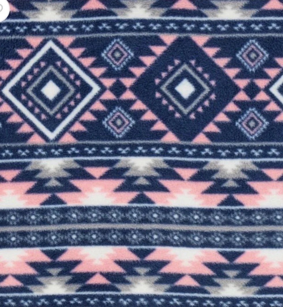 Close-up view of a colorful, geometric-patterned fabric with diamonds, triangles, and stripes in navy blue, pink, white, and beige.