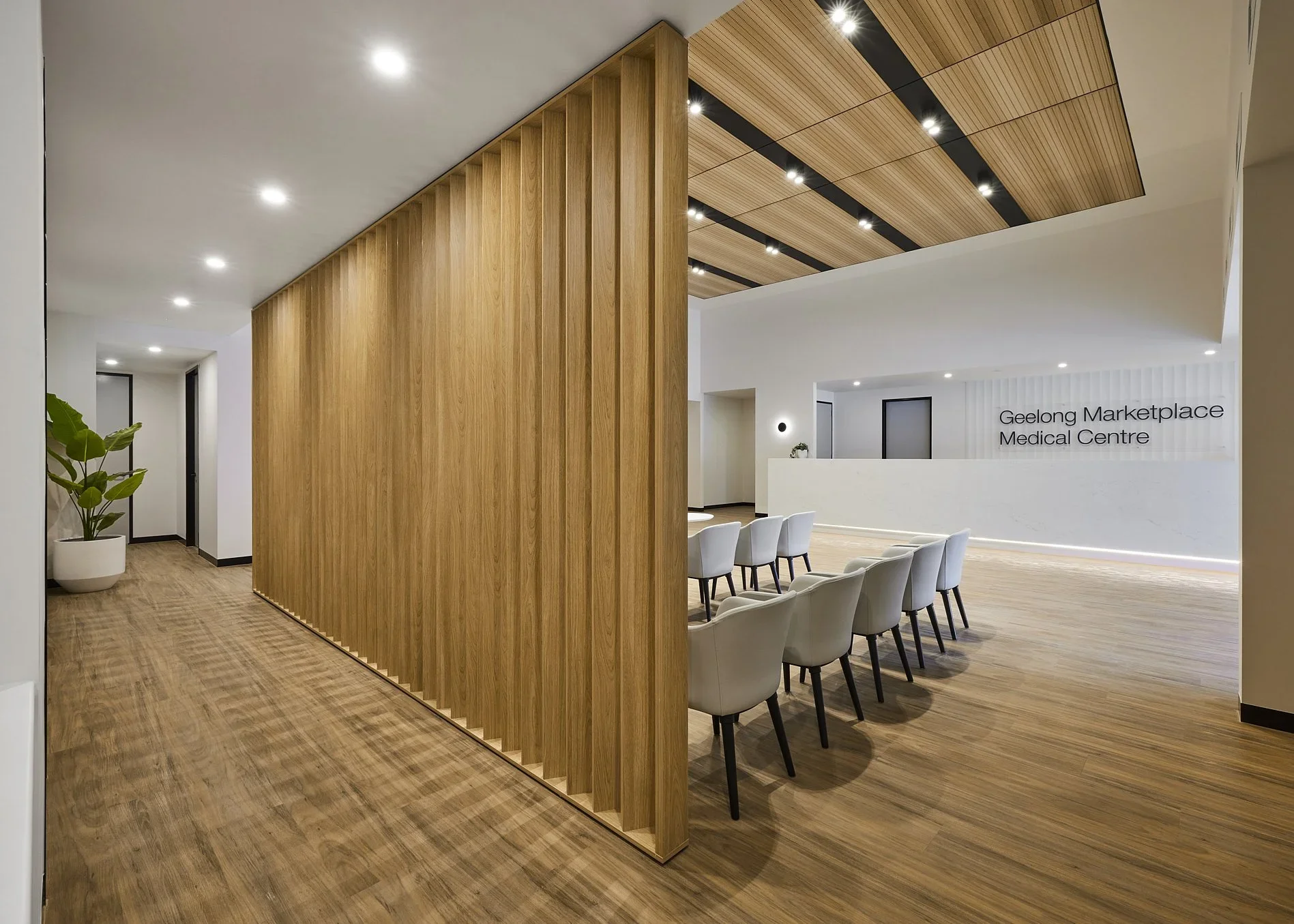 Interior of a medical center lobby with a wooden partition, a row of white chairs, and a sign reading 'Geelong Marketplace Medical Centre'.
