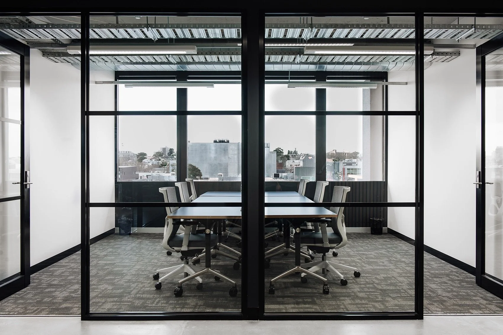 Modern conference room with a long table and ten office chairs, enclosed by glass walls with a city view.