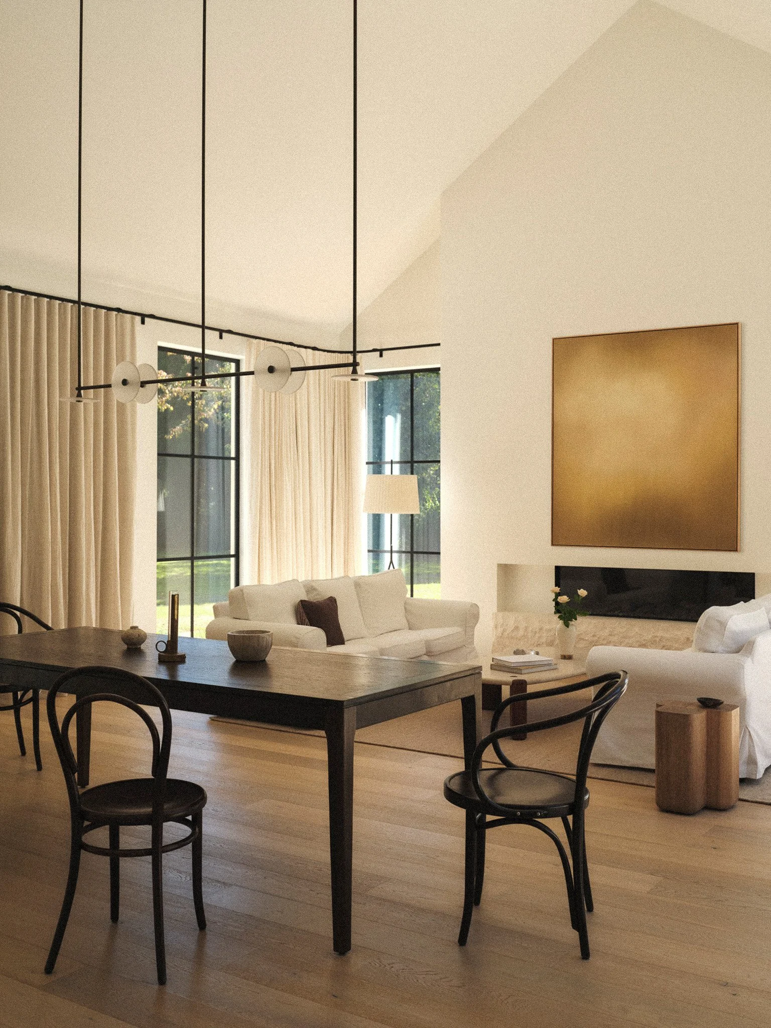 Modern living room with a dining table and chairs, white sofas, large window with curtains, gold wall art above a fireplace, and a mix of decorative items on the table and side table.
