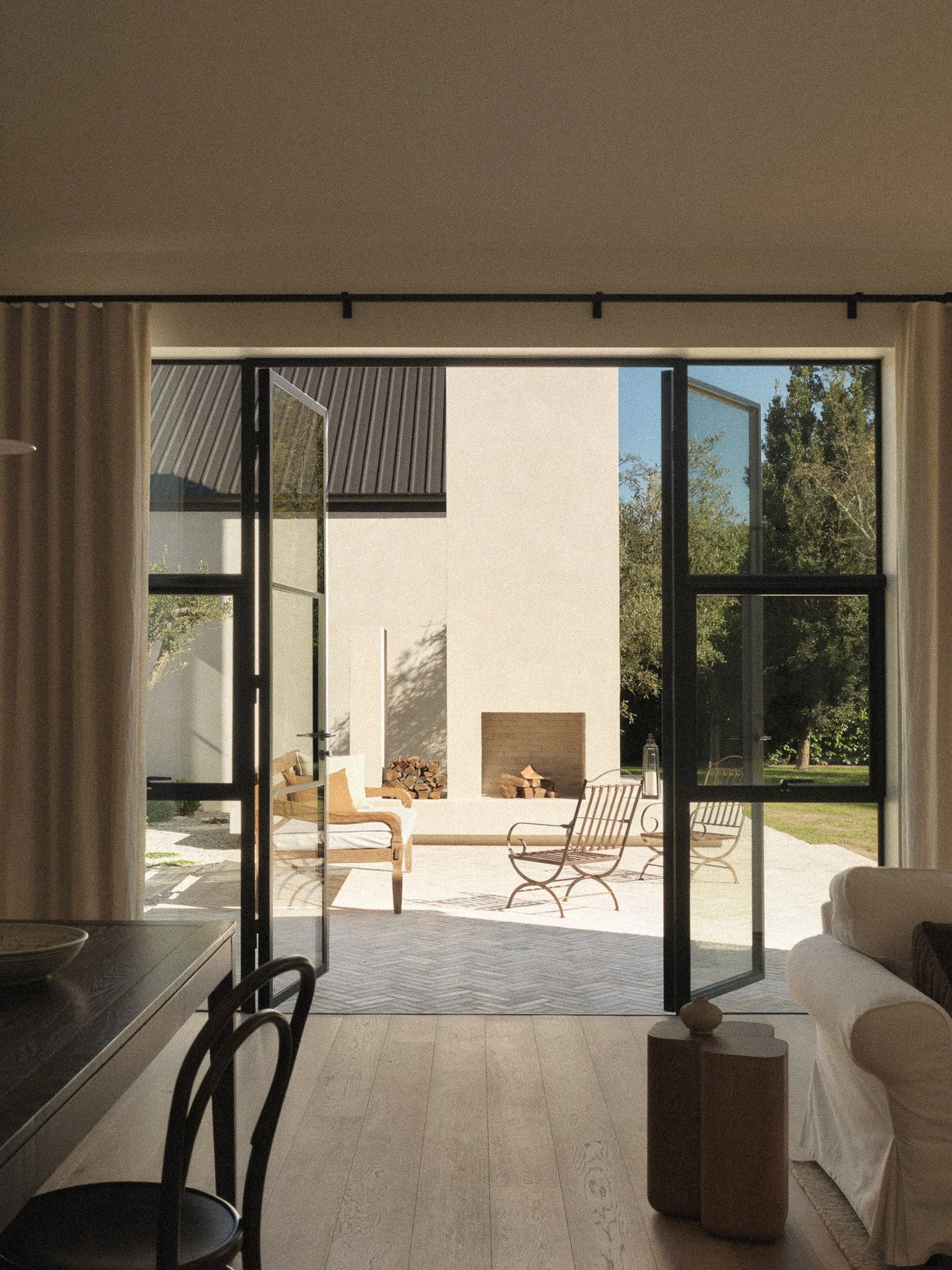 Open glass patio doors leading to an outdoor sitting area with chairs, a small fire pit, and trees in the background under a clear blue sky.