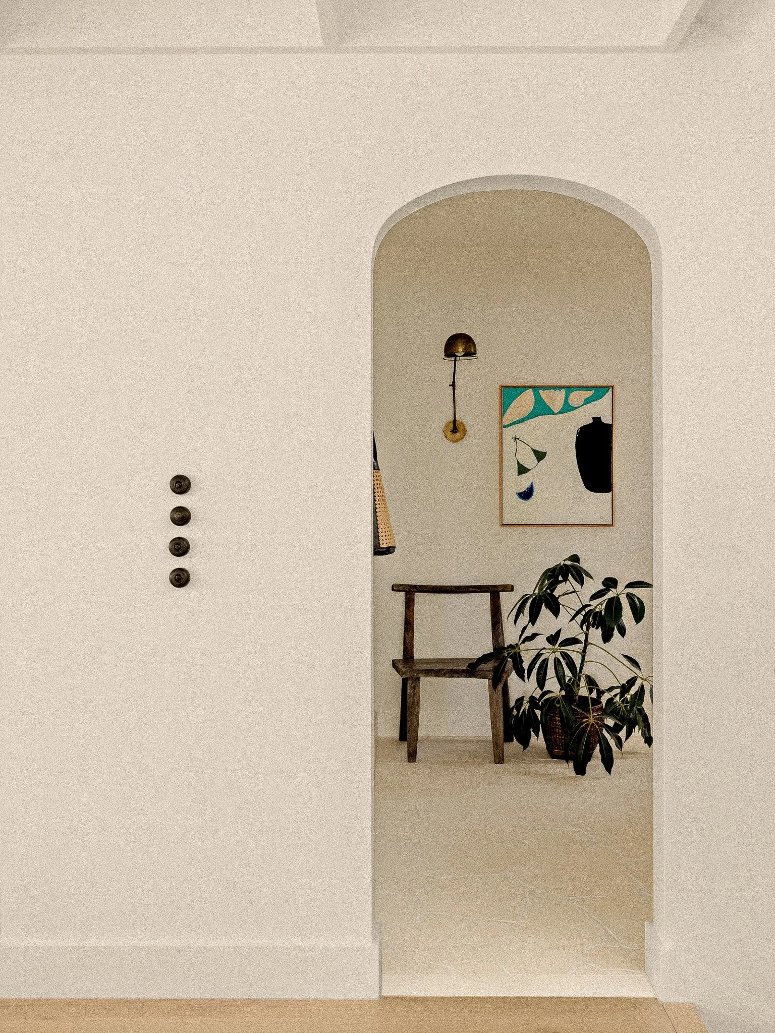 Part of a minimalist modern interior with a small wooden chair, a framed abstract art piece, a wall-mounted lamp, and a potted plant.