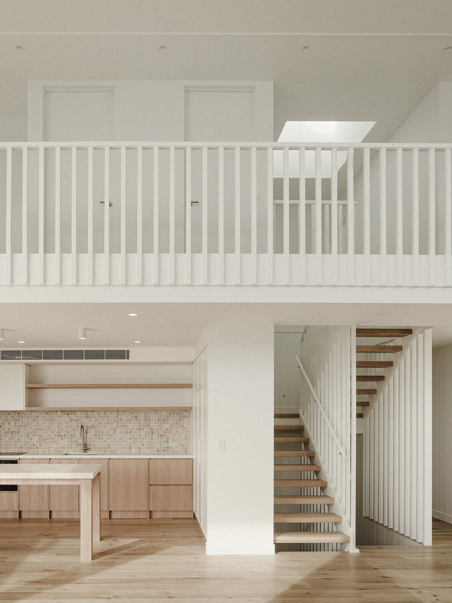 Open-concept kitchen with light wood cabinets, a tiled backsplash, and a staircase with wooden steps and white railing.