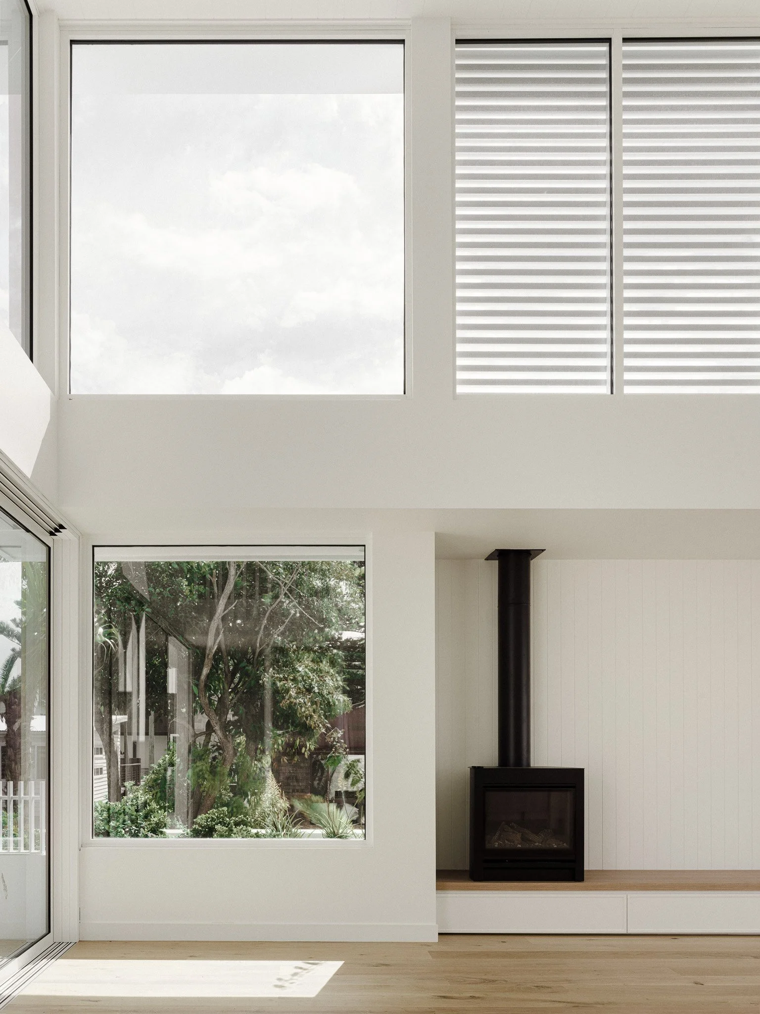 Modern living room with large windows, a black fireplace, and white walls and ceiling.