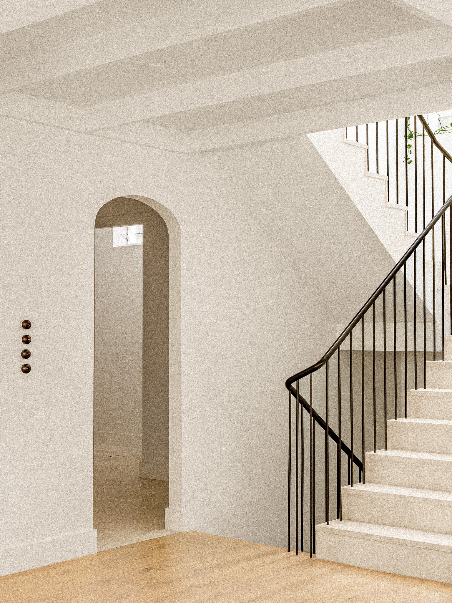 Interior view of a staircase with white steps, black railings, a light-colored wooden floor, and a curved wall with an arched doorway.