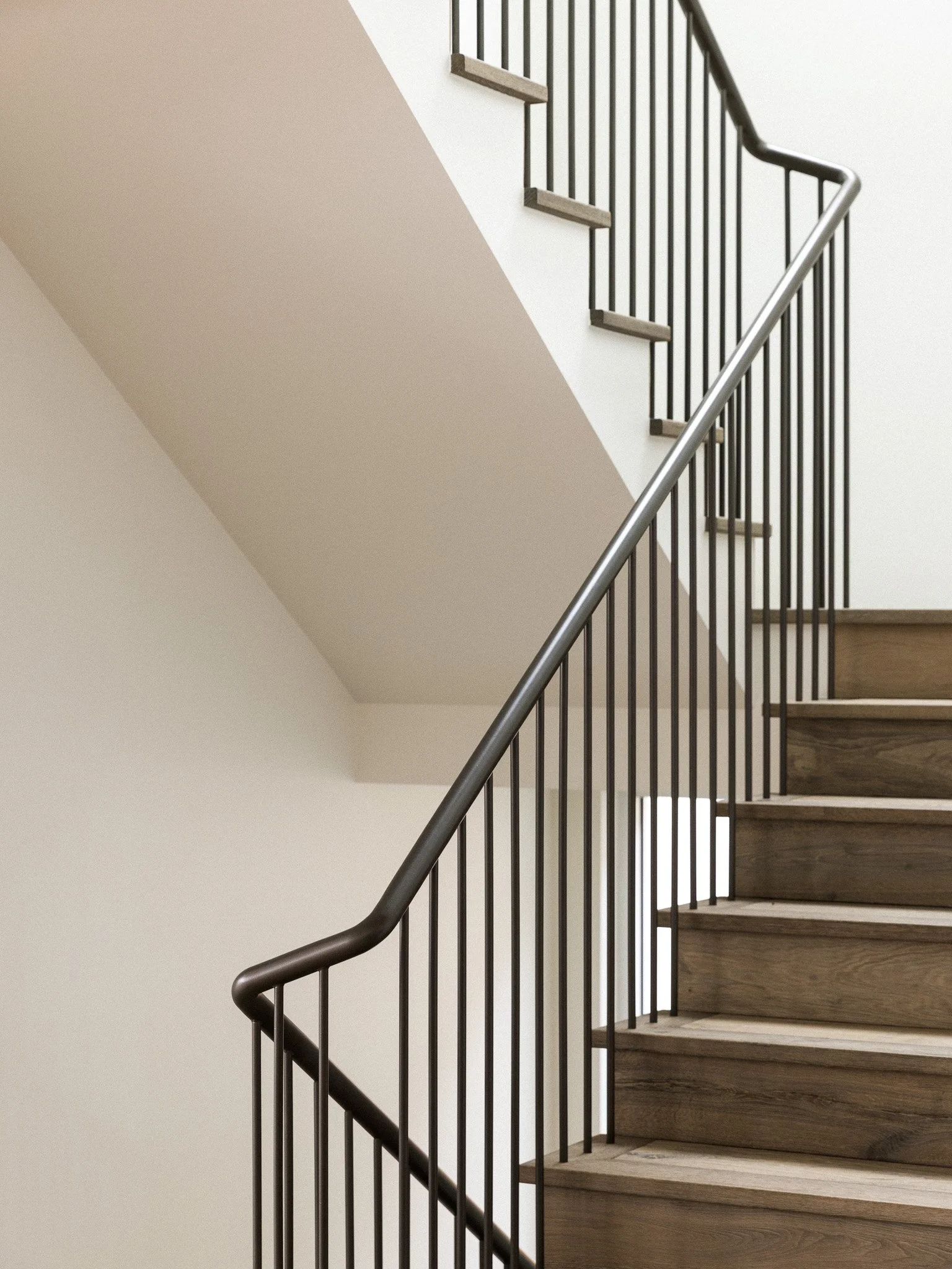 Interior view of a staircase with wooden steps, metal railing, and beige and white walls.