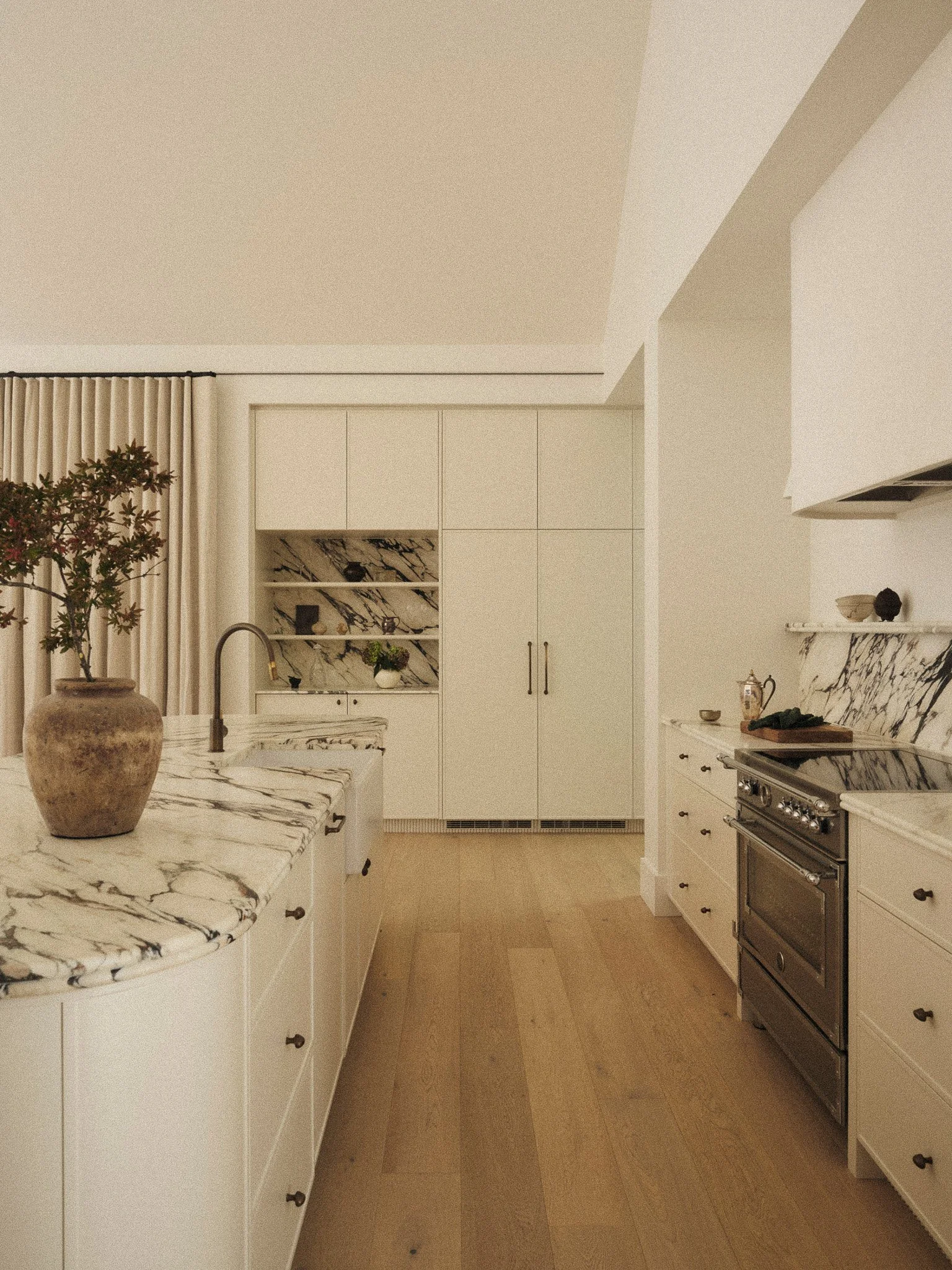 A modern kitchen with white cabinets, a marble countertop, a gas stove, and a potted plant on the counter.