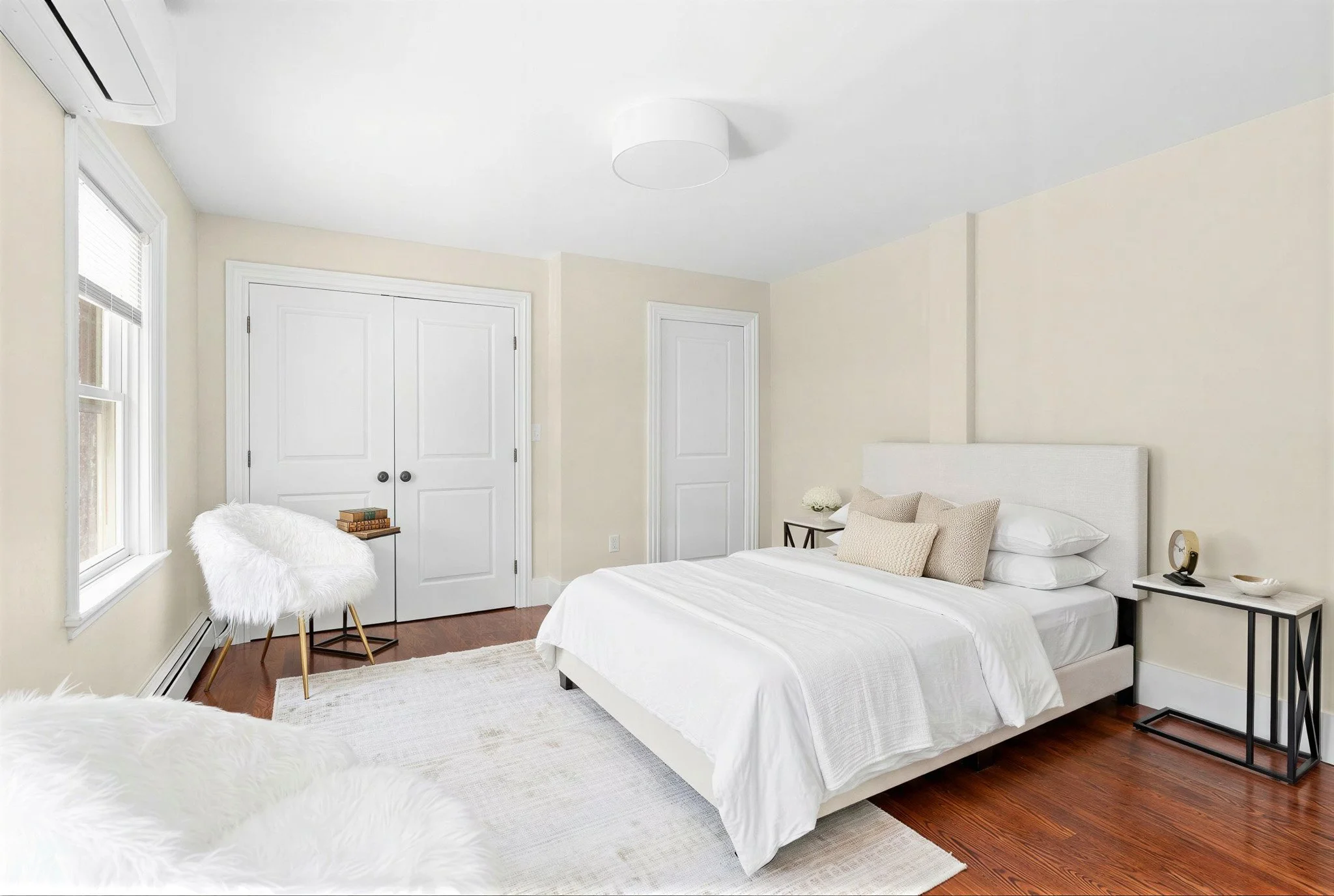 A bedroom with a white bed, nightstand, and minimalist decor, including pillows and a small plant.