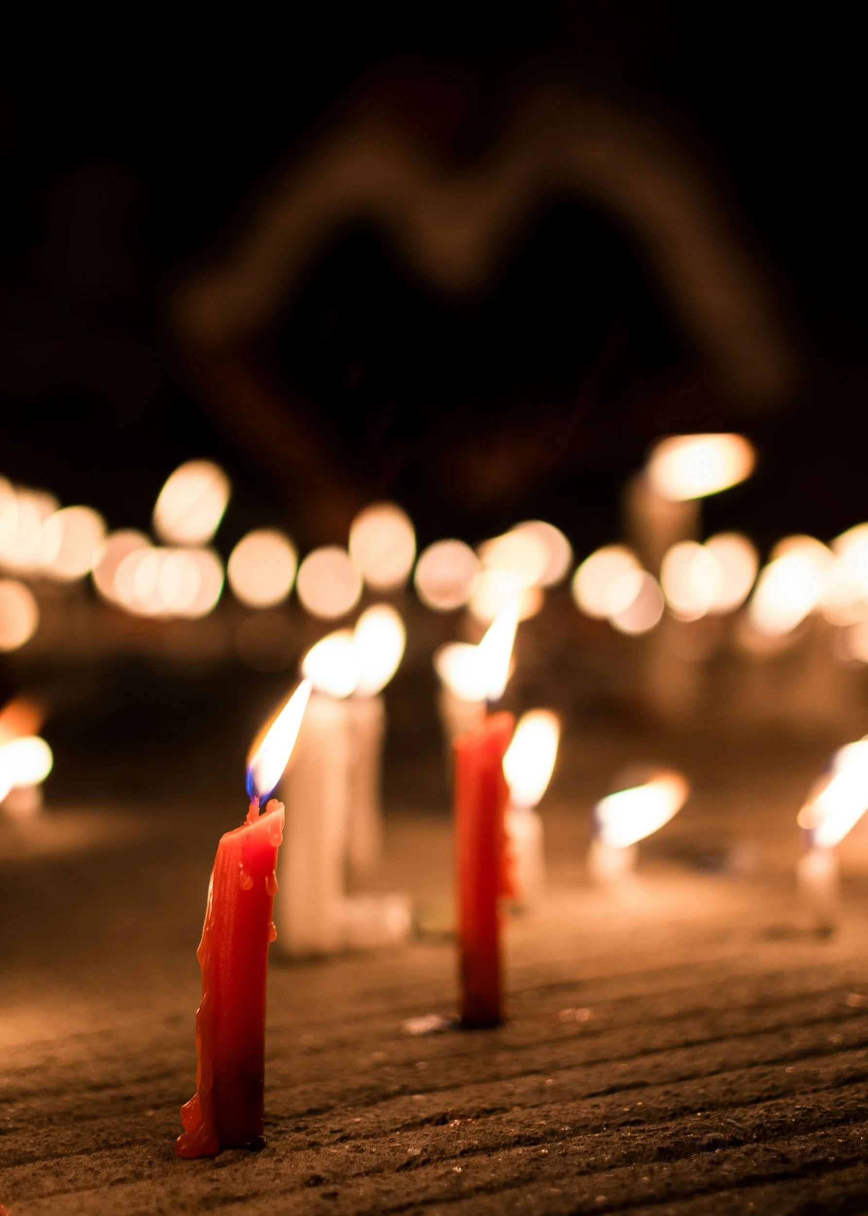 Close-up of withered candles on a wooden surface, with blurred warm candles in the background.