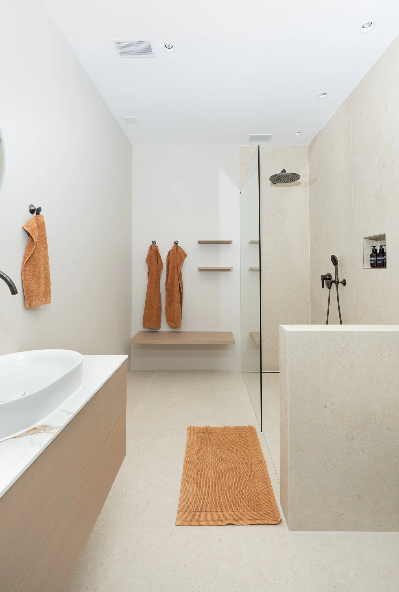 Modernes Badezimmer mit einer begehbaren Dusche, einer weißen Badewanne, Holzregalen, Handtüchern in Orangetönen, Fliesenboden und -wänden in neutralen Farbtönen, sowie einem großen Wandspiegel.