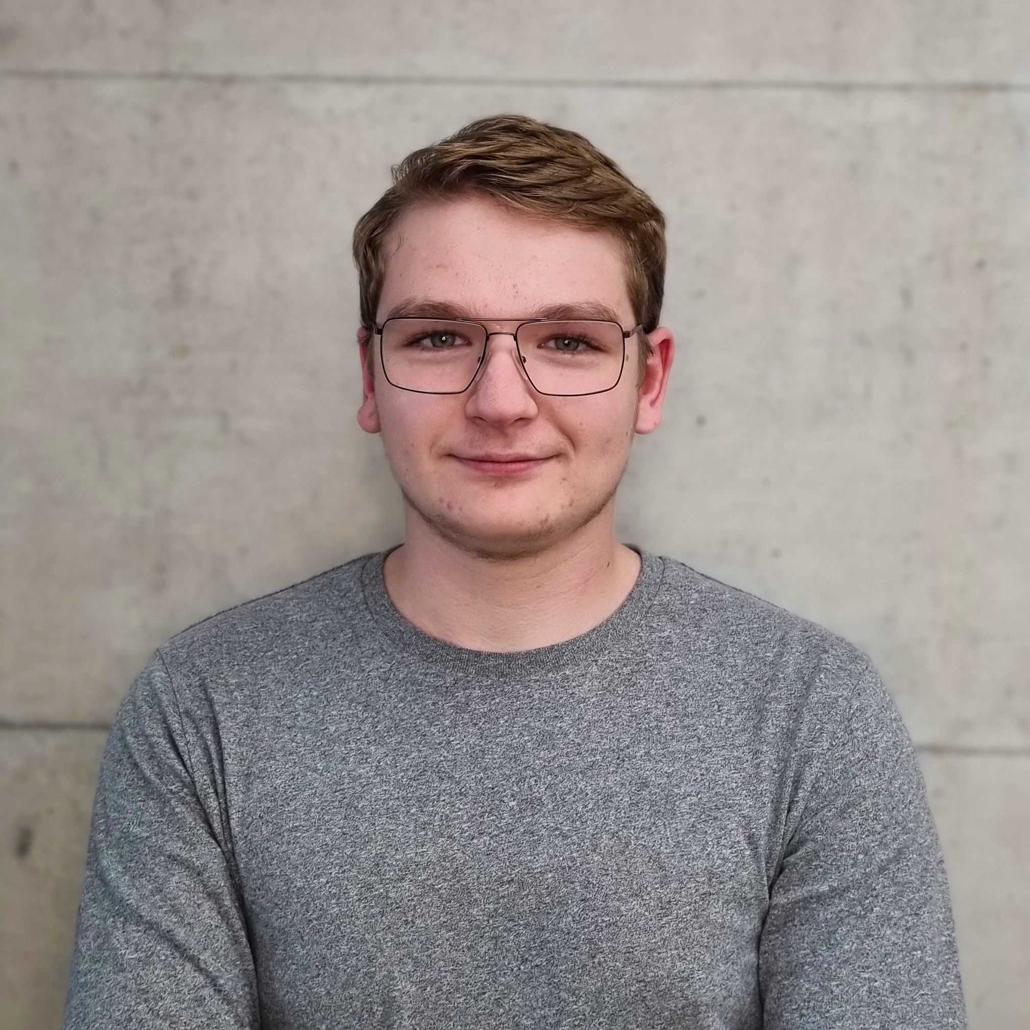 Porträt von Yanik Schrag, Planung, Zeichner EFZ Architektur, Techniker HF Architektur in Ausbildung, vor einer hellen Betonwand.