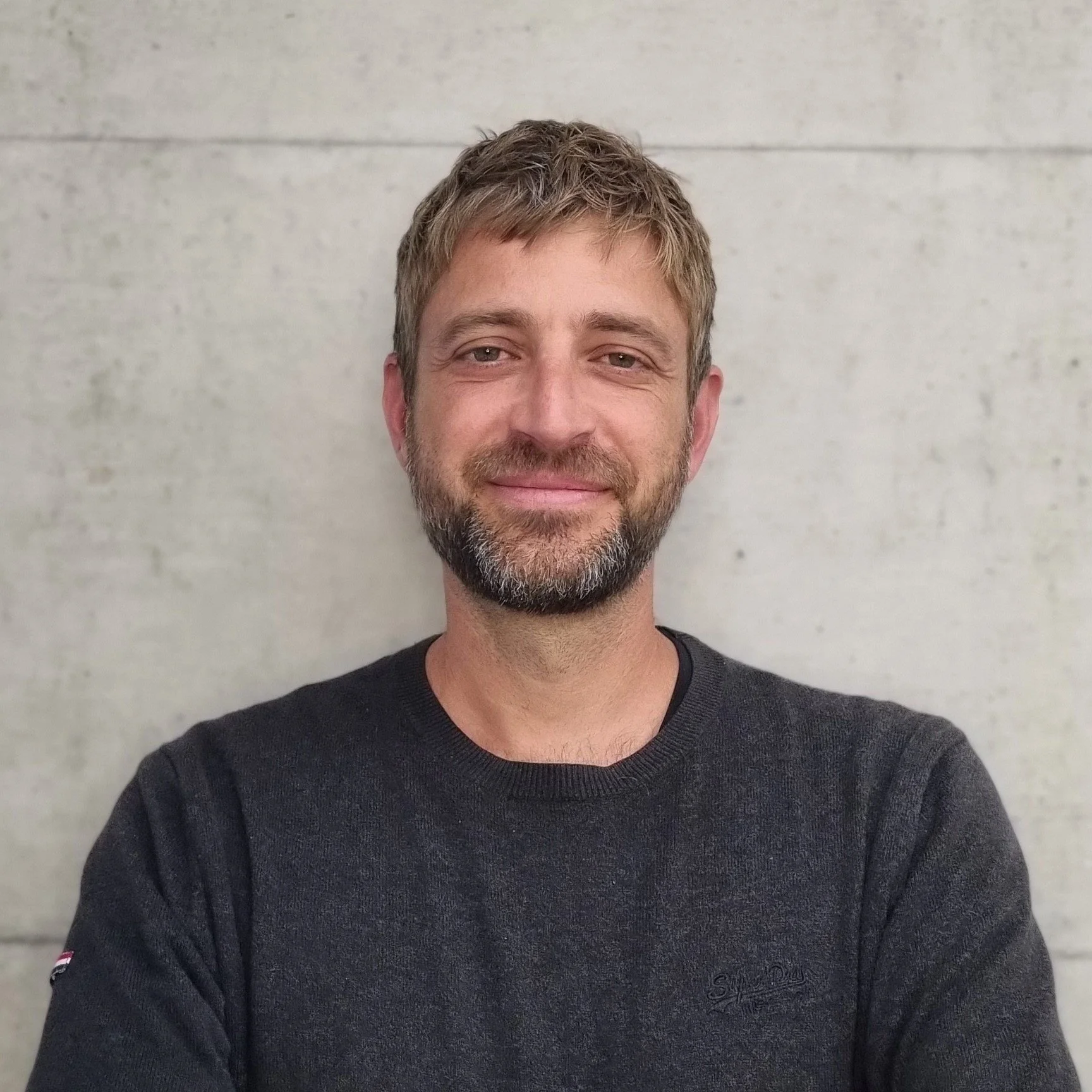 Porträt von Simon Bissegger, Mitglied der Geschäftsleitung, Projektleitung, dipl. Bauleiter,  vor einer hellen Betonwand.
