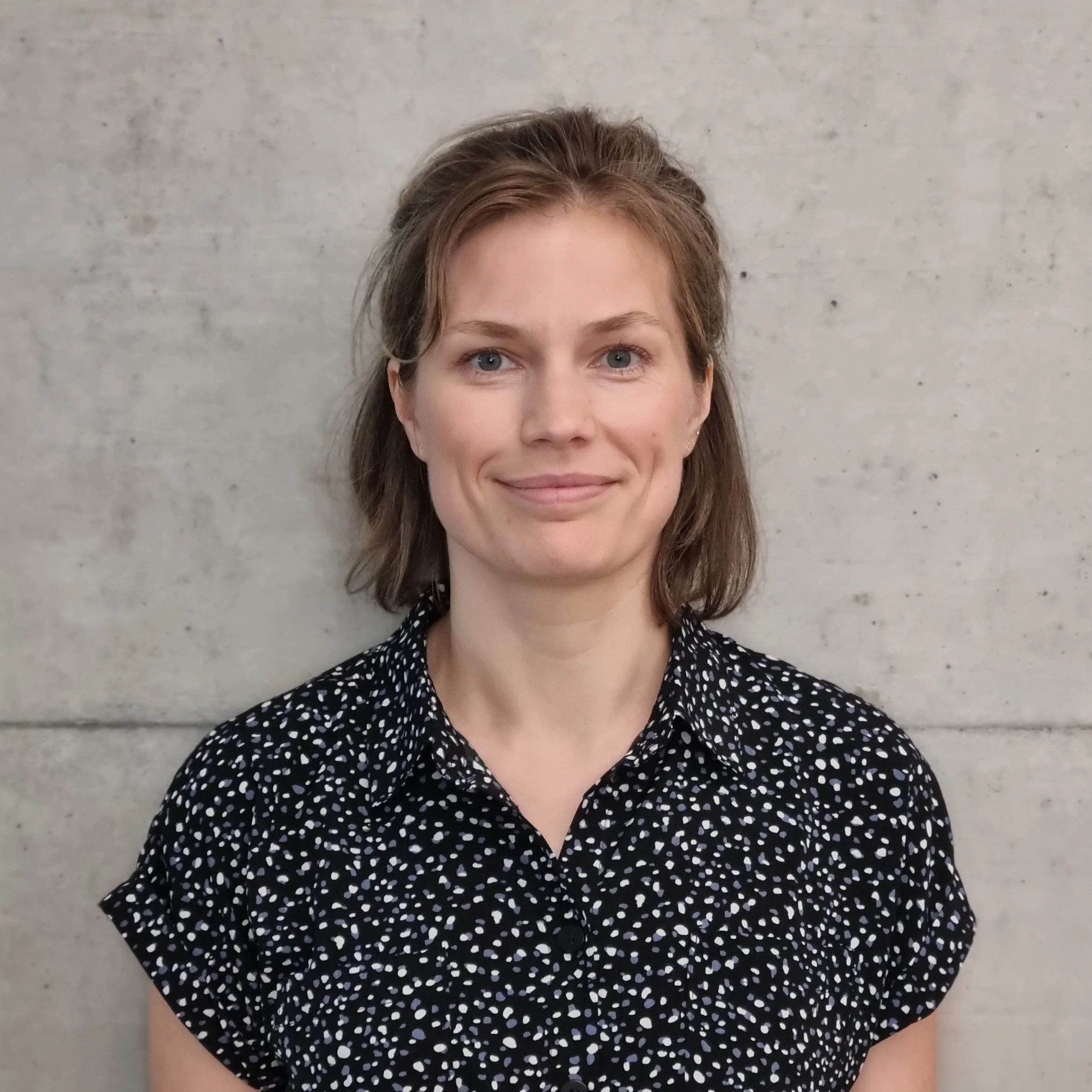 Porträt von Katerina Rakach, Entwurf, Architektin MA, vor einer hellen Betonwand.