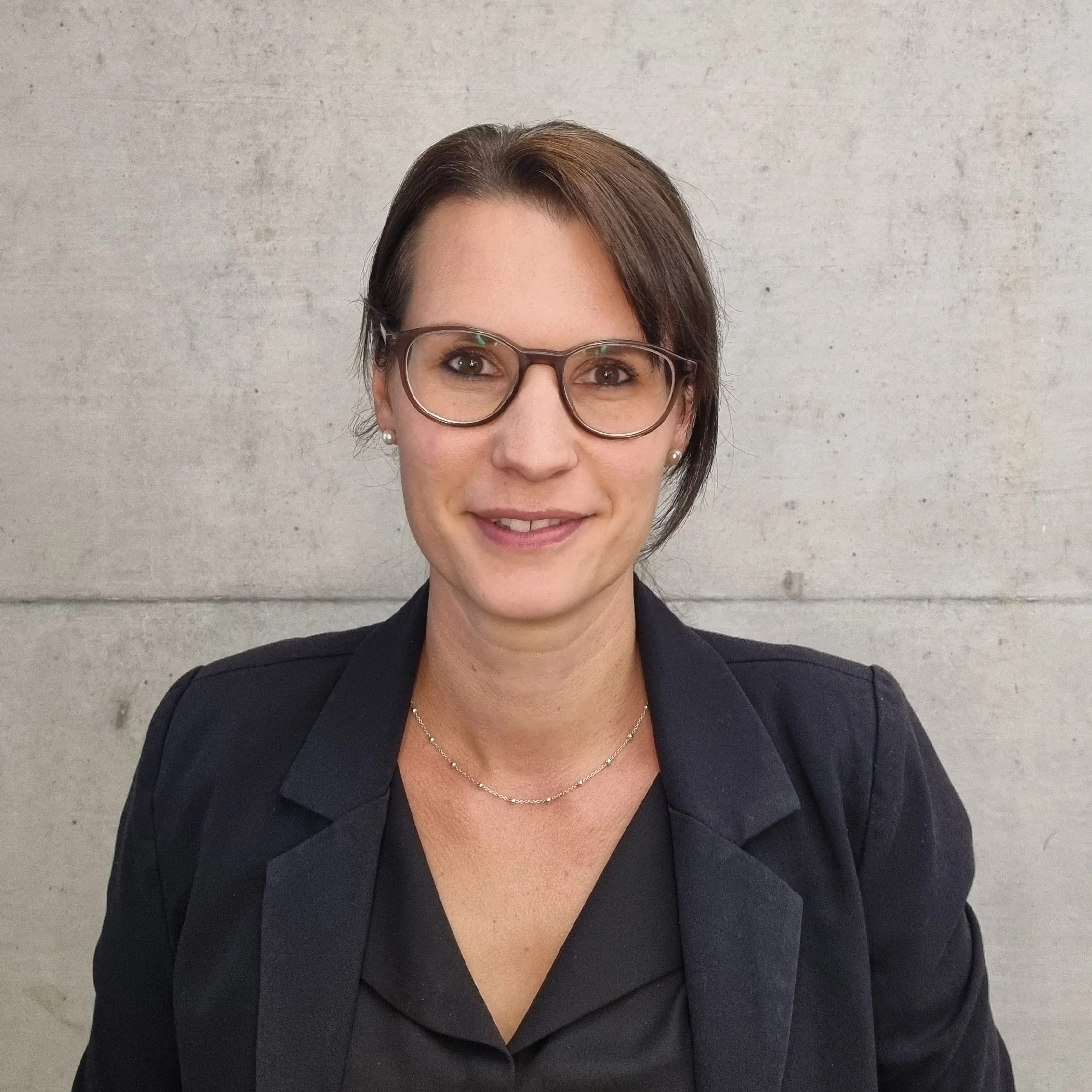 Porträt von Stefanie Spahr, Mitglied der Geschäftsleitung, und Architektin BA | EMBA vor einer hellgrauen Betonwand.