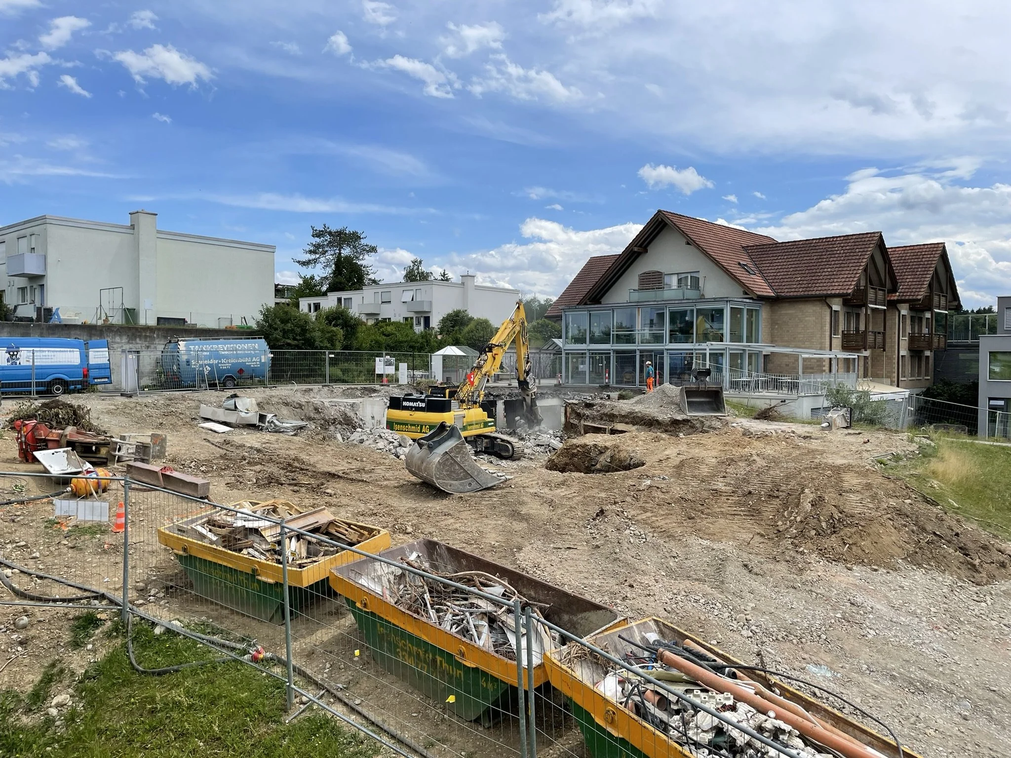 Baustelle mit Baugeräten, Zäunen und Häusern im Hintergrund bei schönem Himmel.