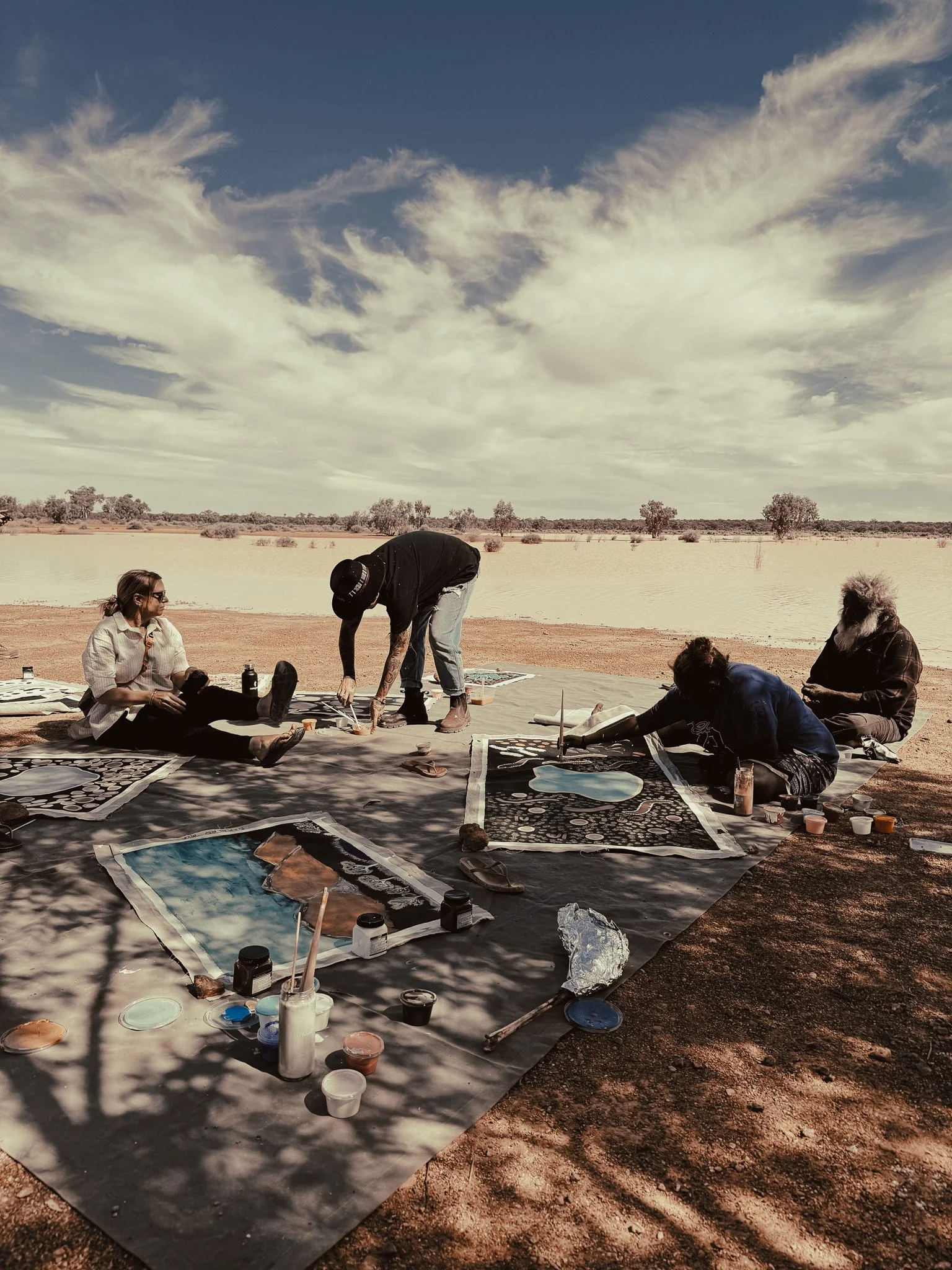 First Nation Australians painting by a fresh water lake in the remote outback of Australia